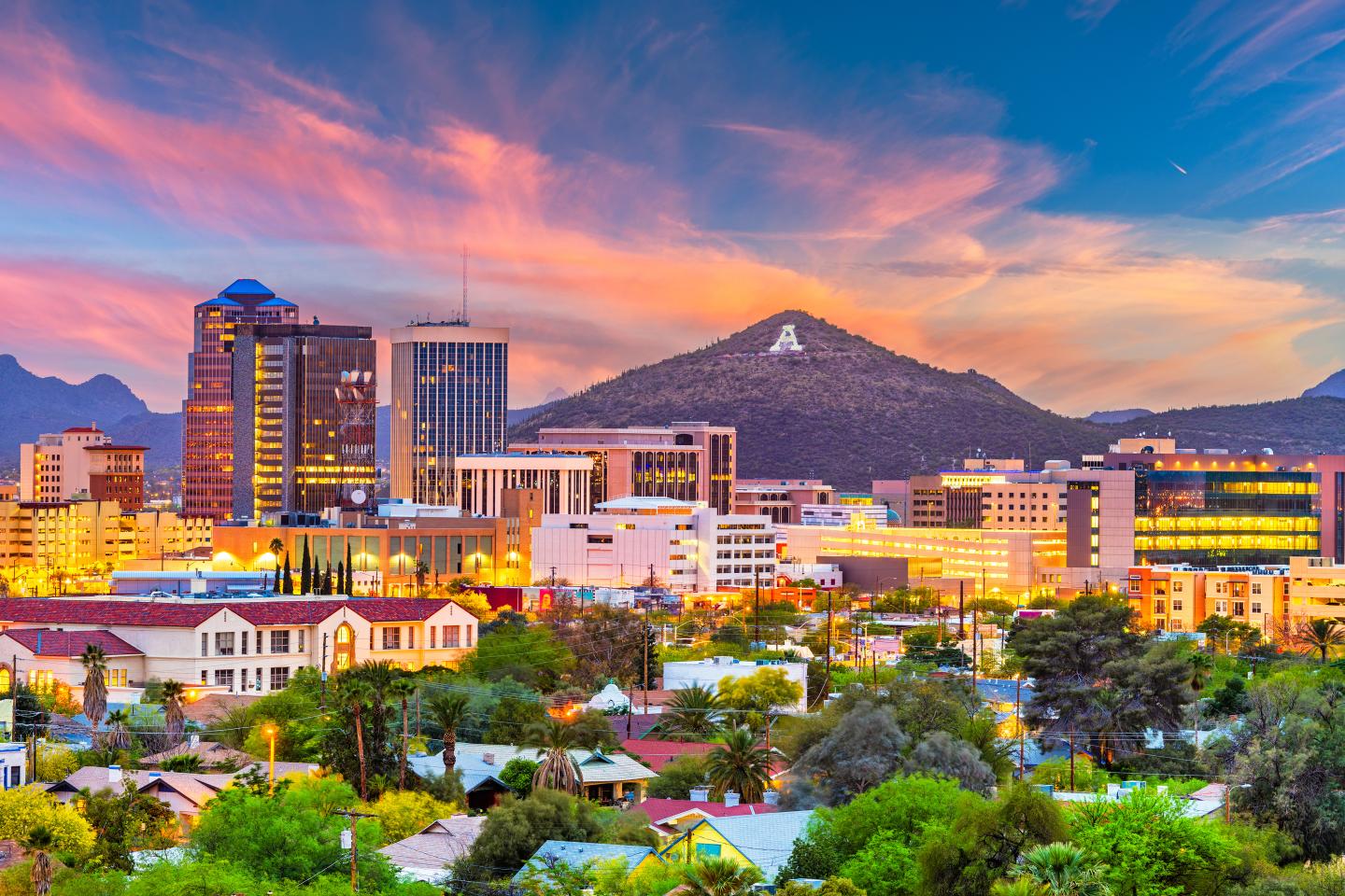Tucson skyline with mountains at sunset, colorful sky, buildings illuminated.