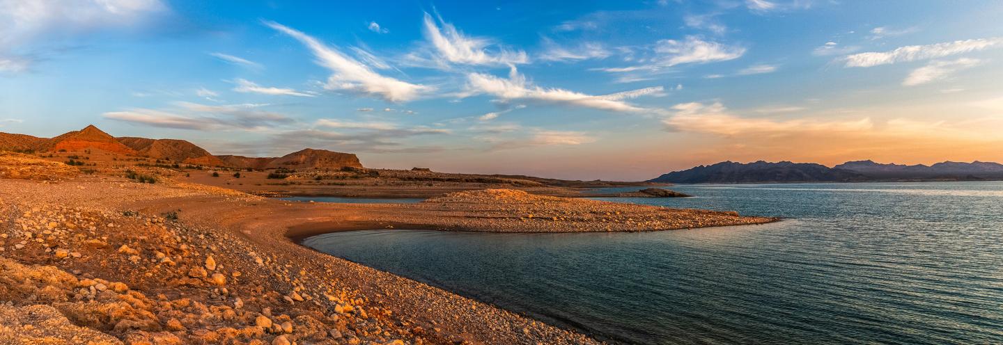 Rocky shoreline with clear blue sky and distant mountains at sunset.