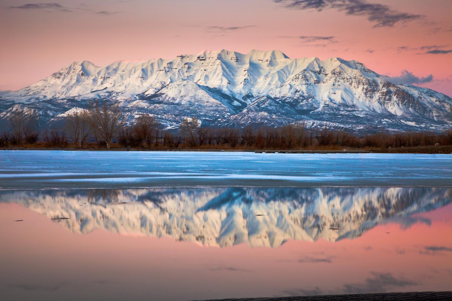 Snowy mountains and their reflection in a tranquil lake at sunset.