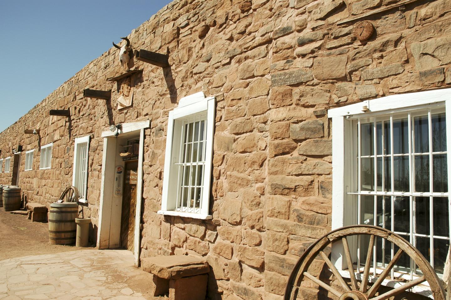 Trading post building with white window frames, barrels, and a wooden wagon wheel outside.