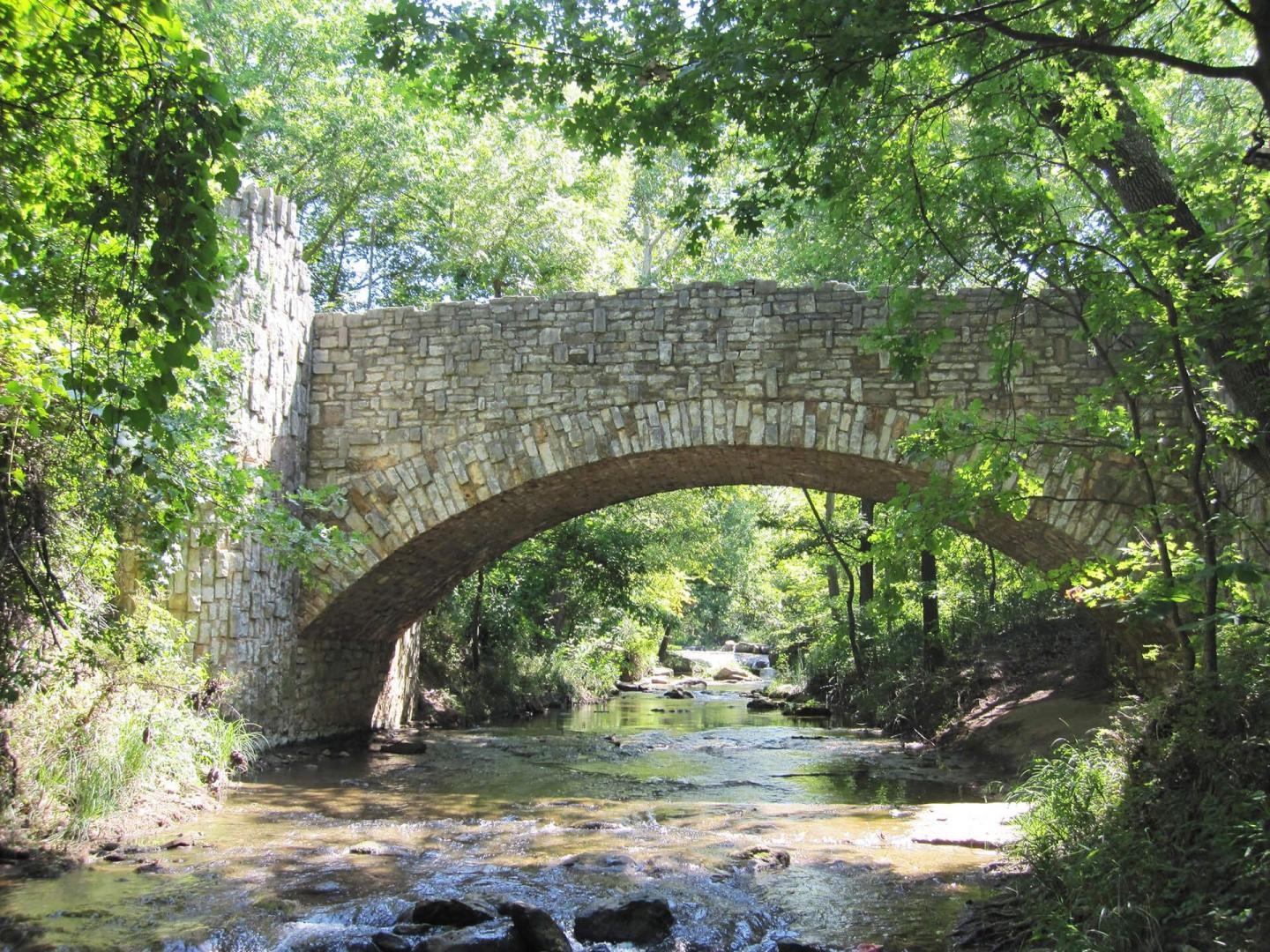 Stone bridge over a sunlit forest stream.