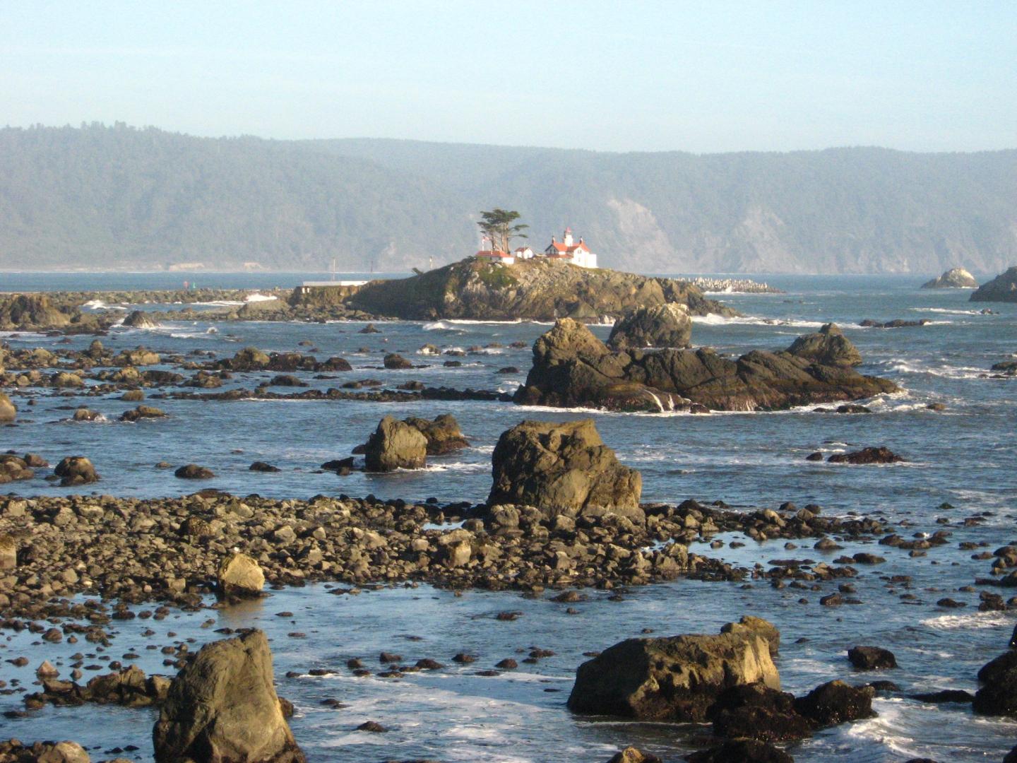 Rocky seashore with distant lighthouse on an island.