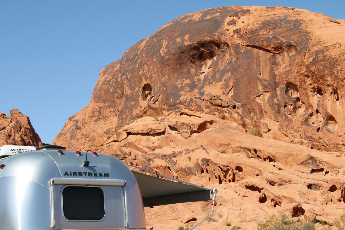 Silver trailer near orange rock formations under clear blue sky.