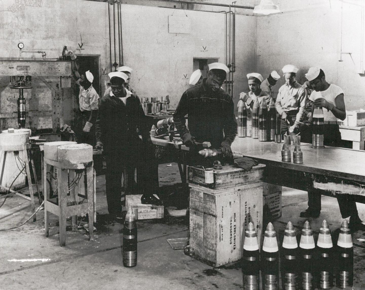 Black and white photo of workers in a factory assembling artillery shells.