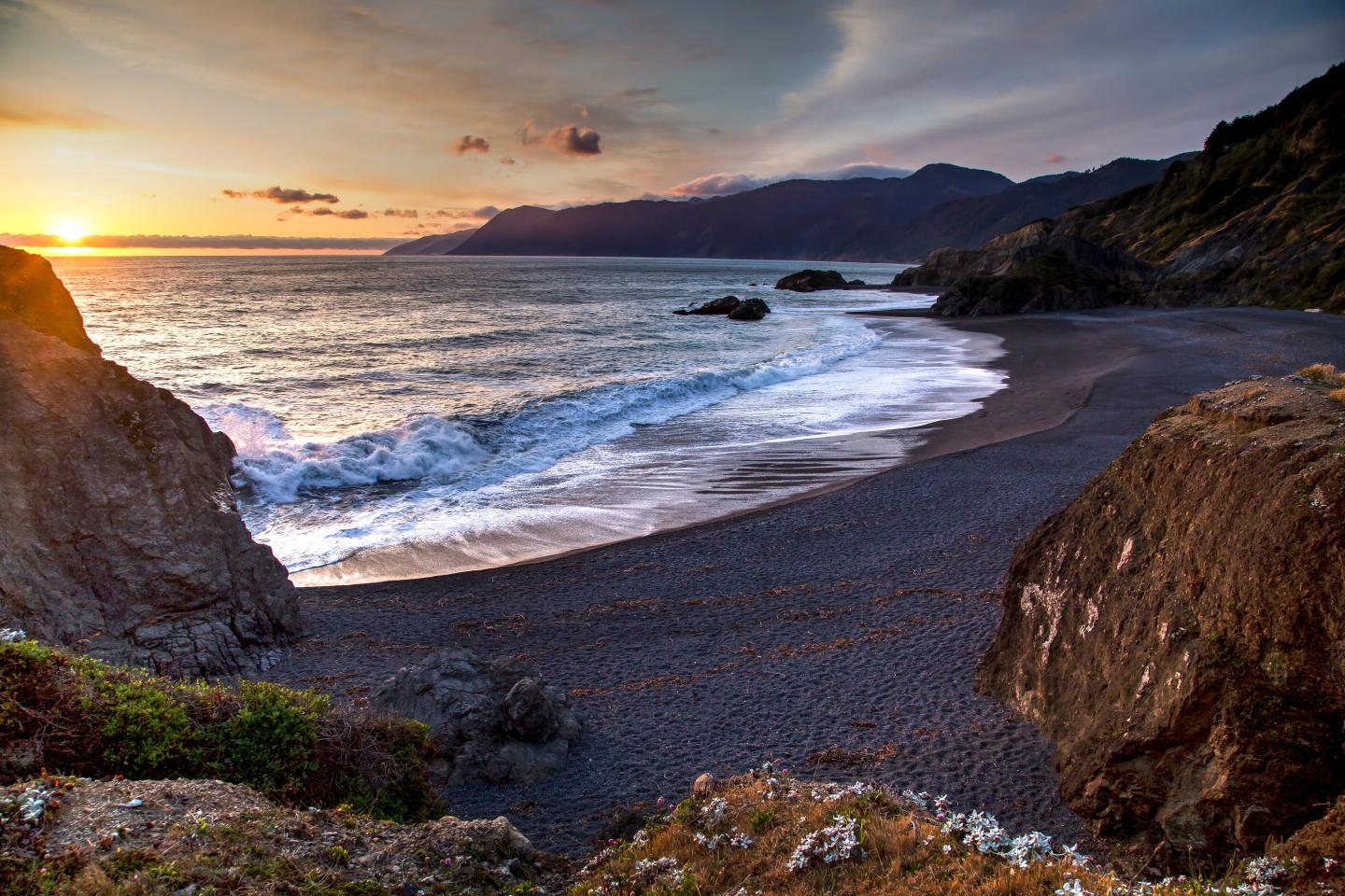 A Lost Coast beach at sunset with waves crashing and distant mountains.