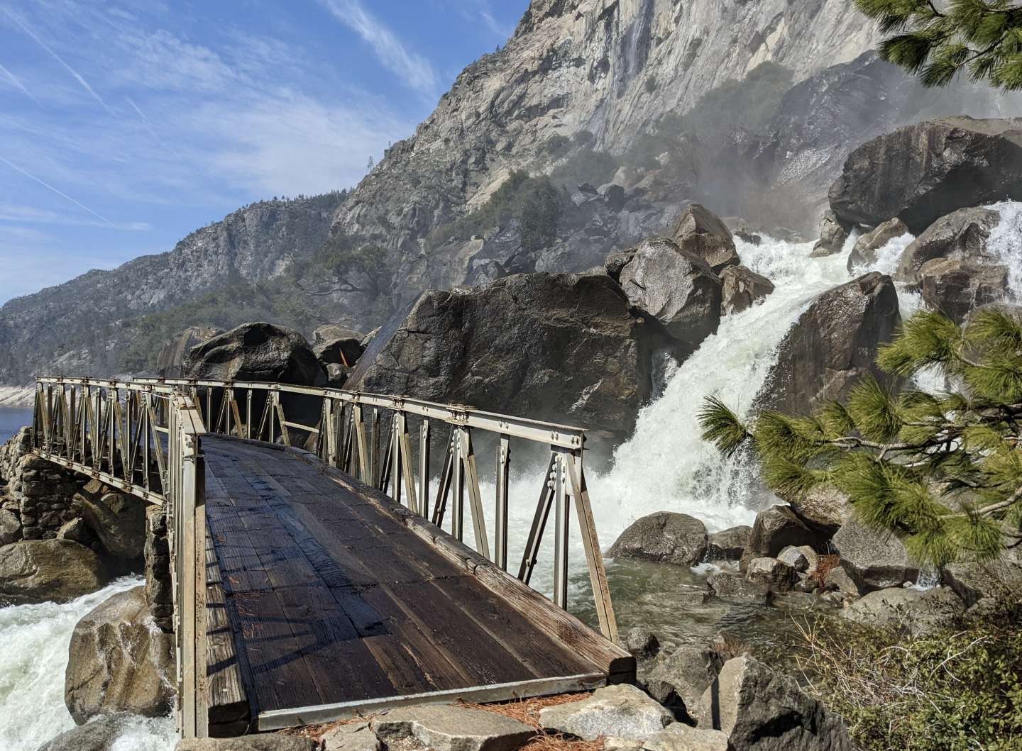 Wapama Falls bridge over a rushing waterfall, mountains in the background.