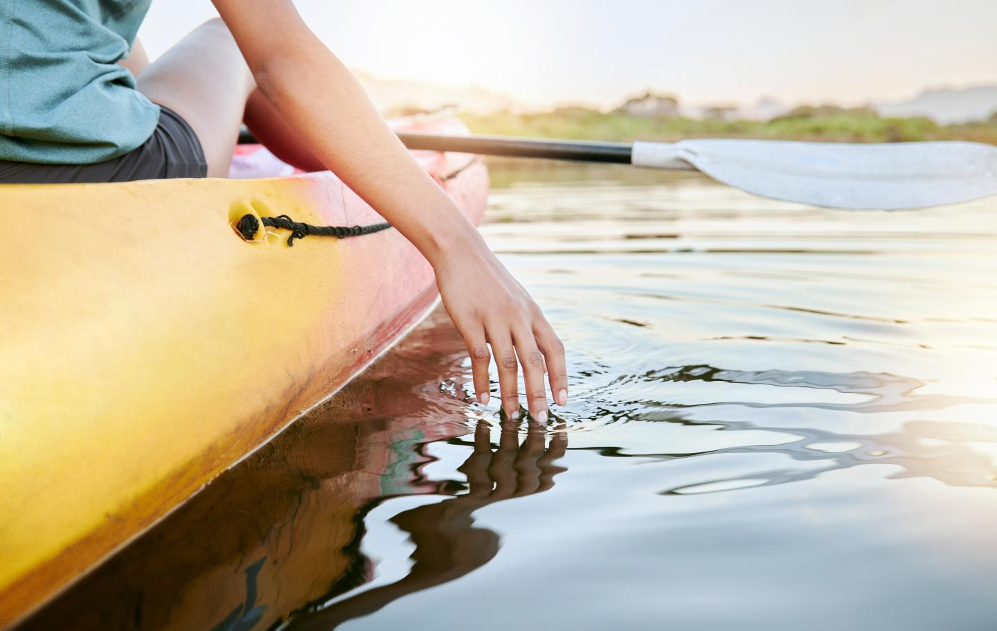 Kayaker's hand touching water, bright and calm setting.