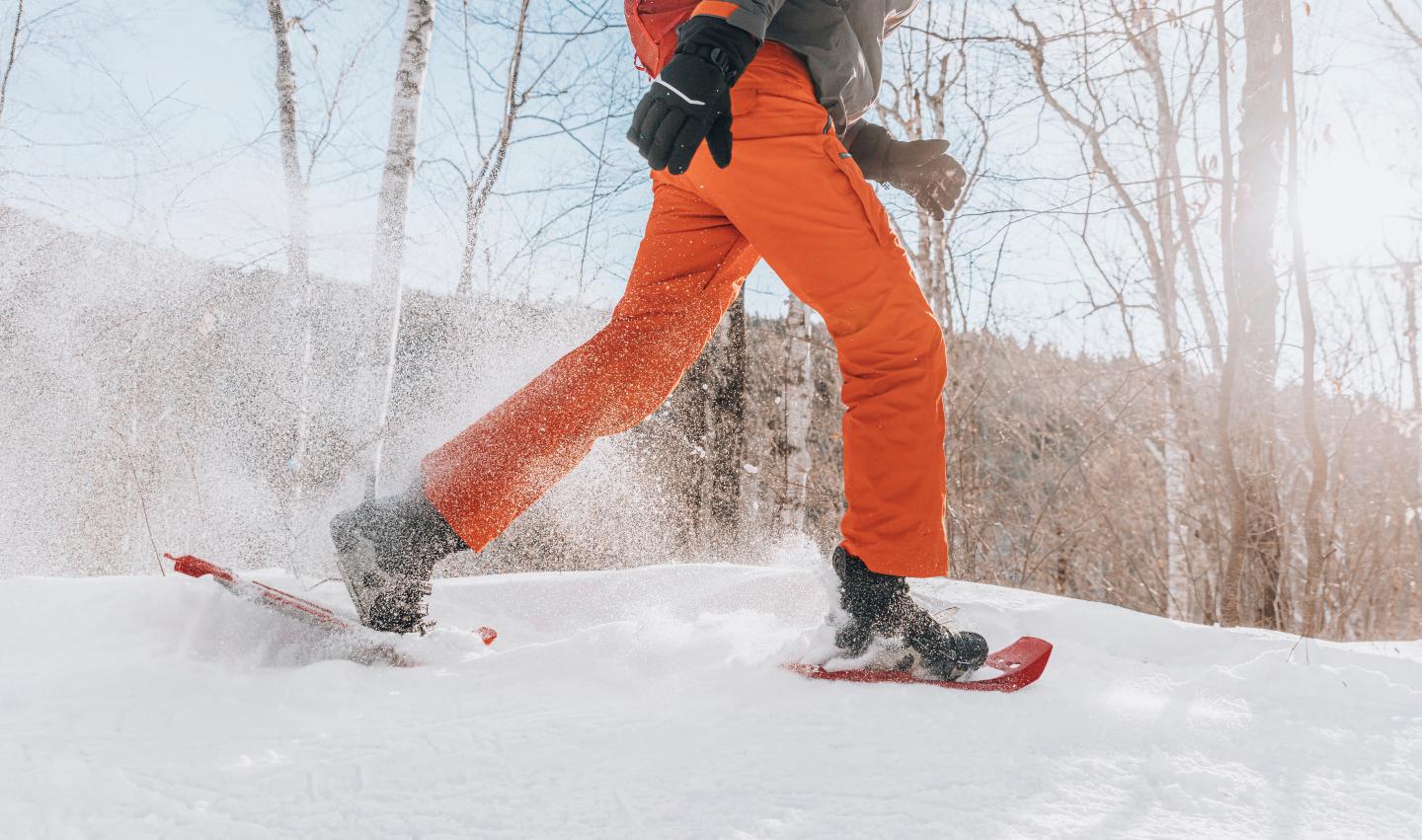Snowshoer in orange pants walking through snowy forest.