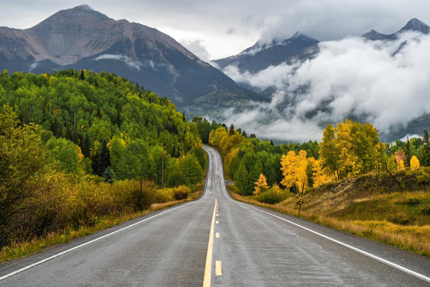 Long road leading through forested mountains under cloudy skies.