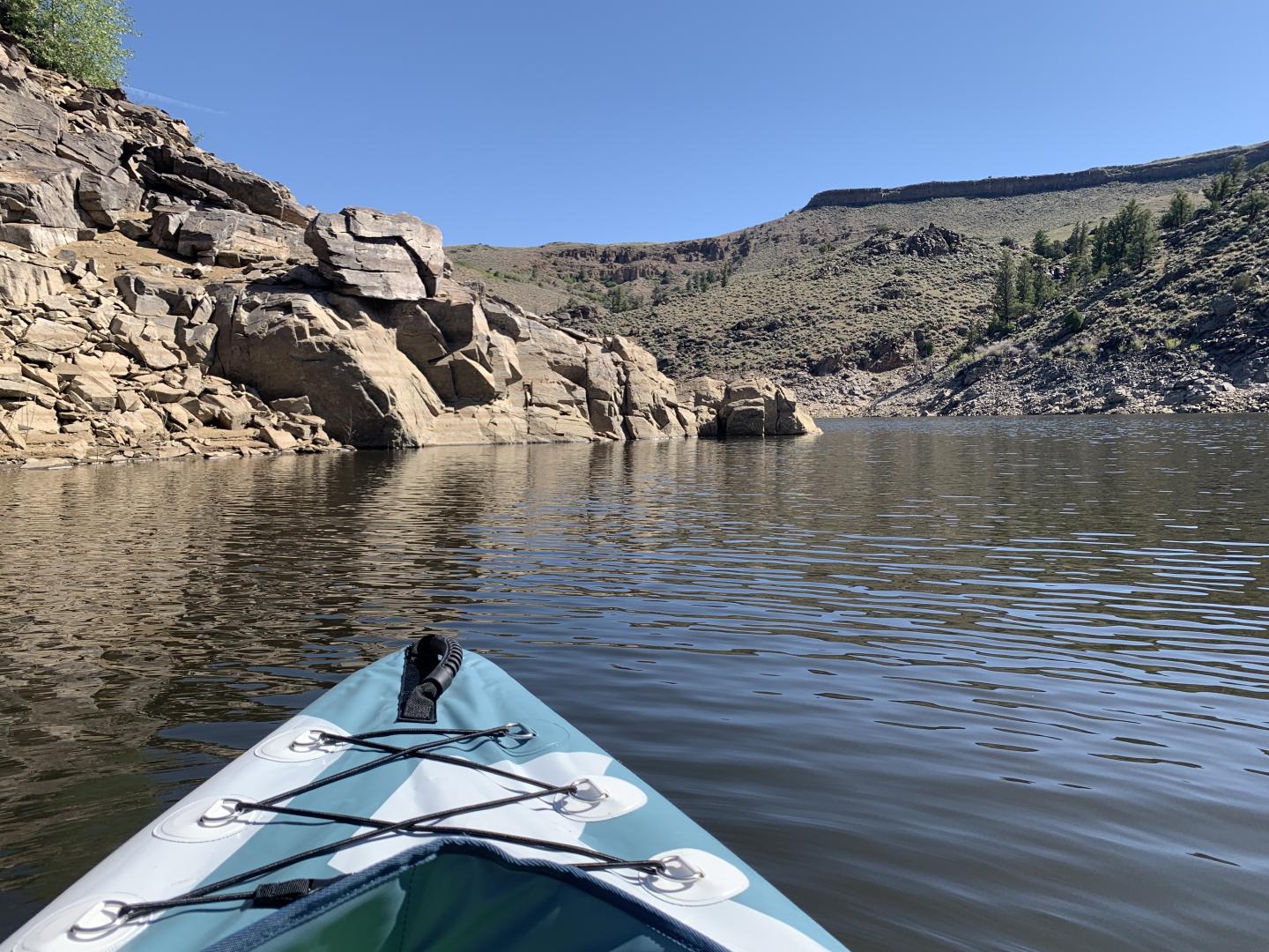 Kayak on calm lake near rocky cliff under clear blue sky.