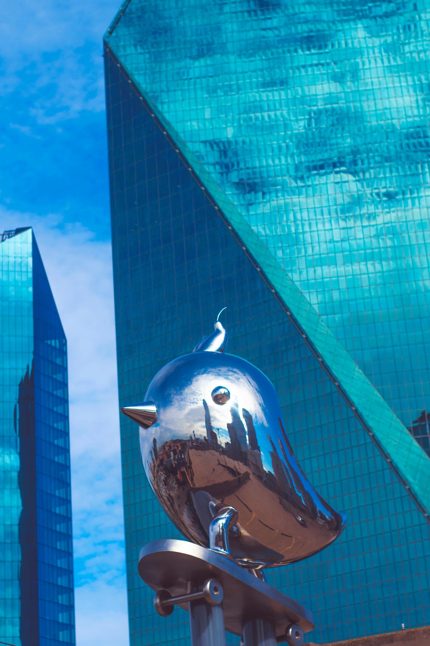 Shiny metal bird sculpture against tall glass buildings.