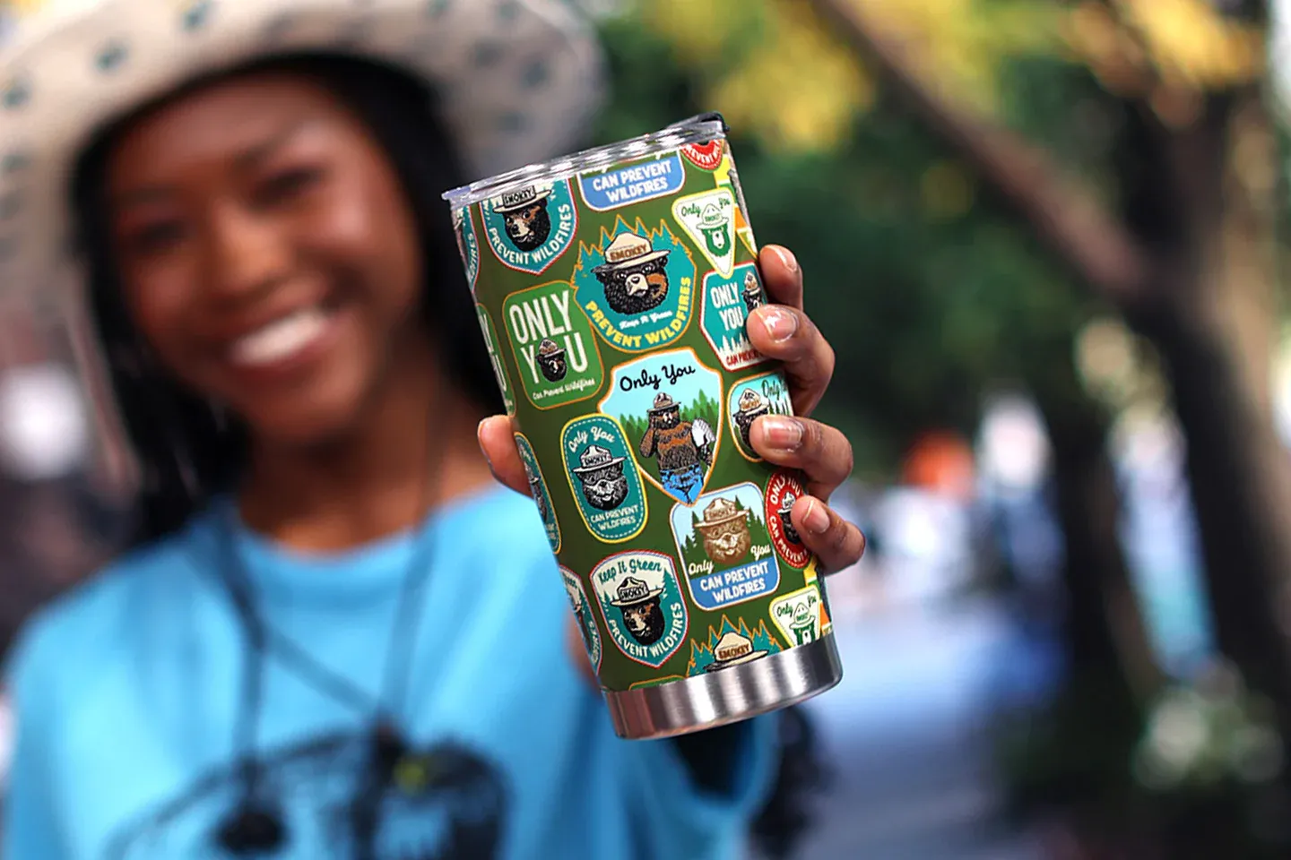 Smiling person holding a decorated tumbler outdoors.