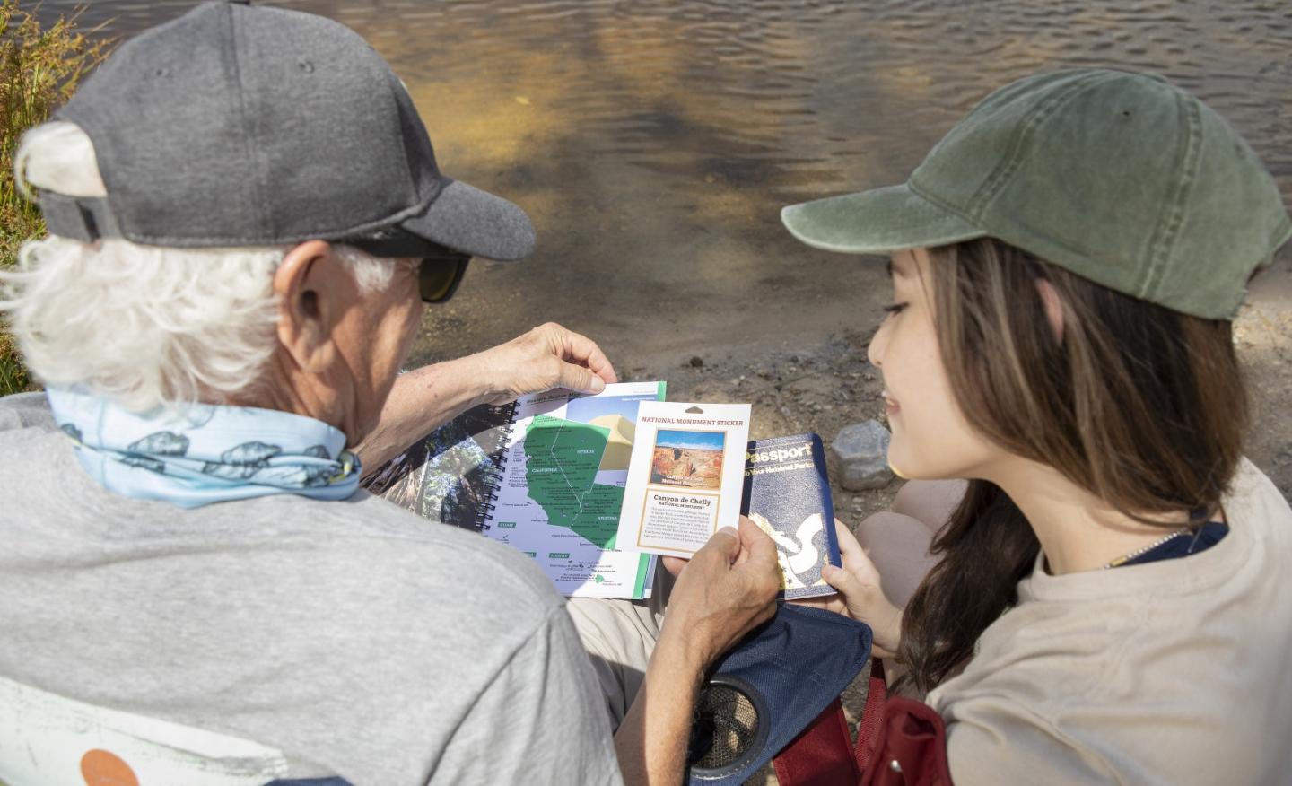 Older man and young woman reading a map by a riverbank.