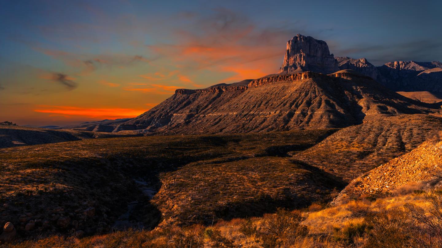 Sunset over rugged desert mountains with a vibrant sky.