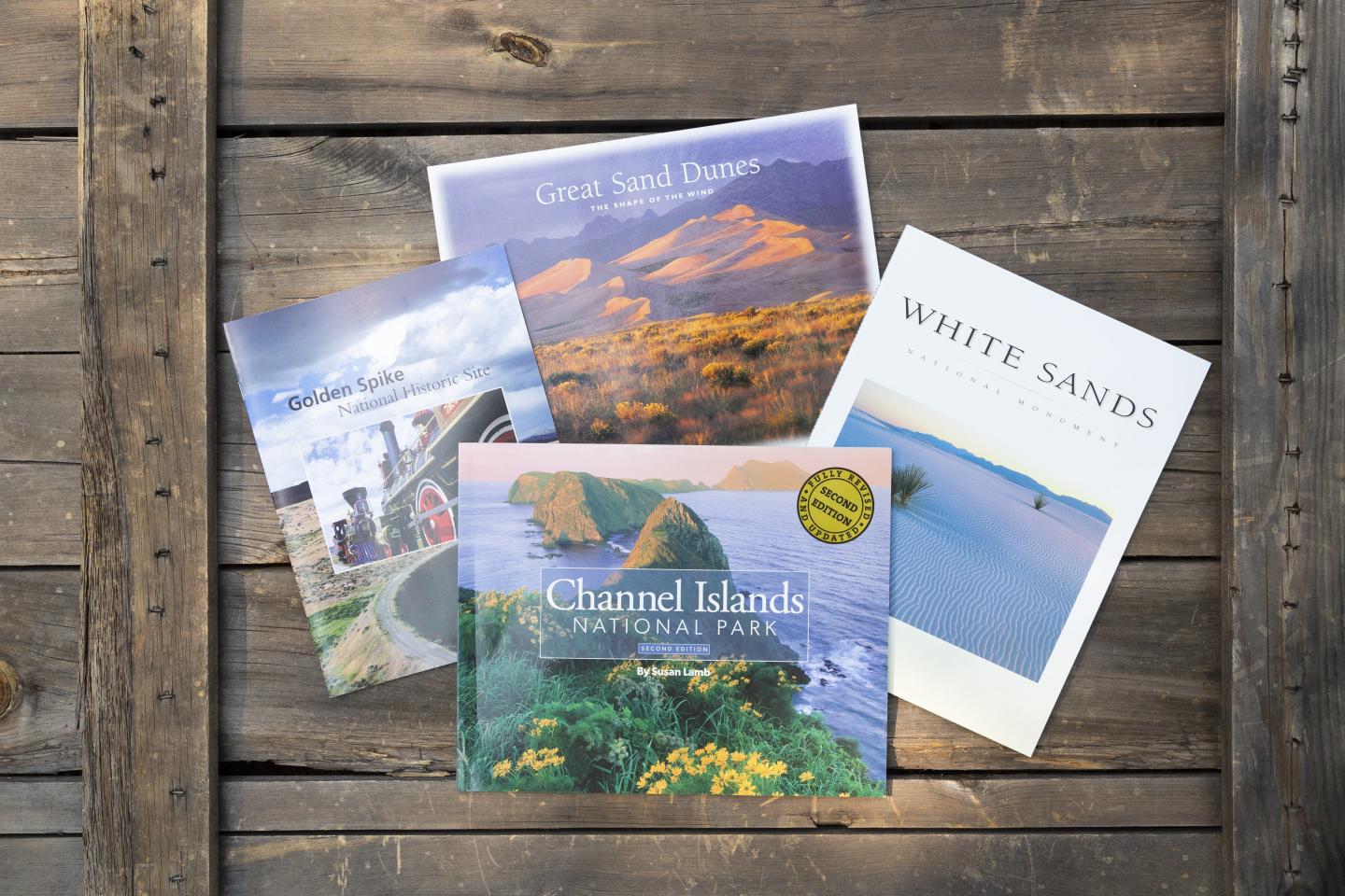 Four colorful landscape photo books on a wooden surface.