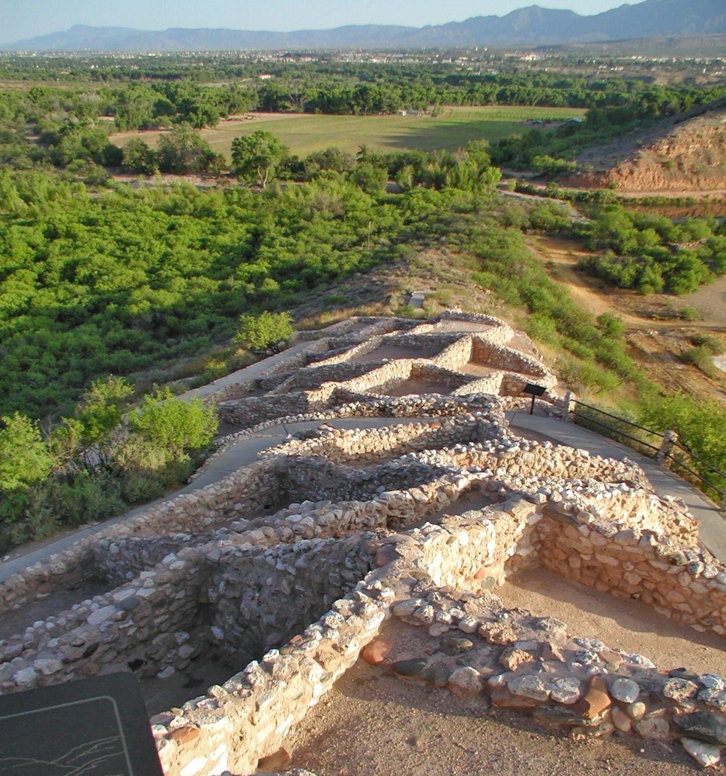 Stone ruins on a hillside with lush green fields and distant mountains.