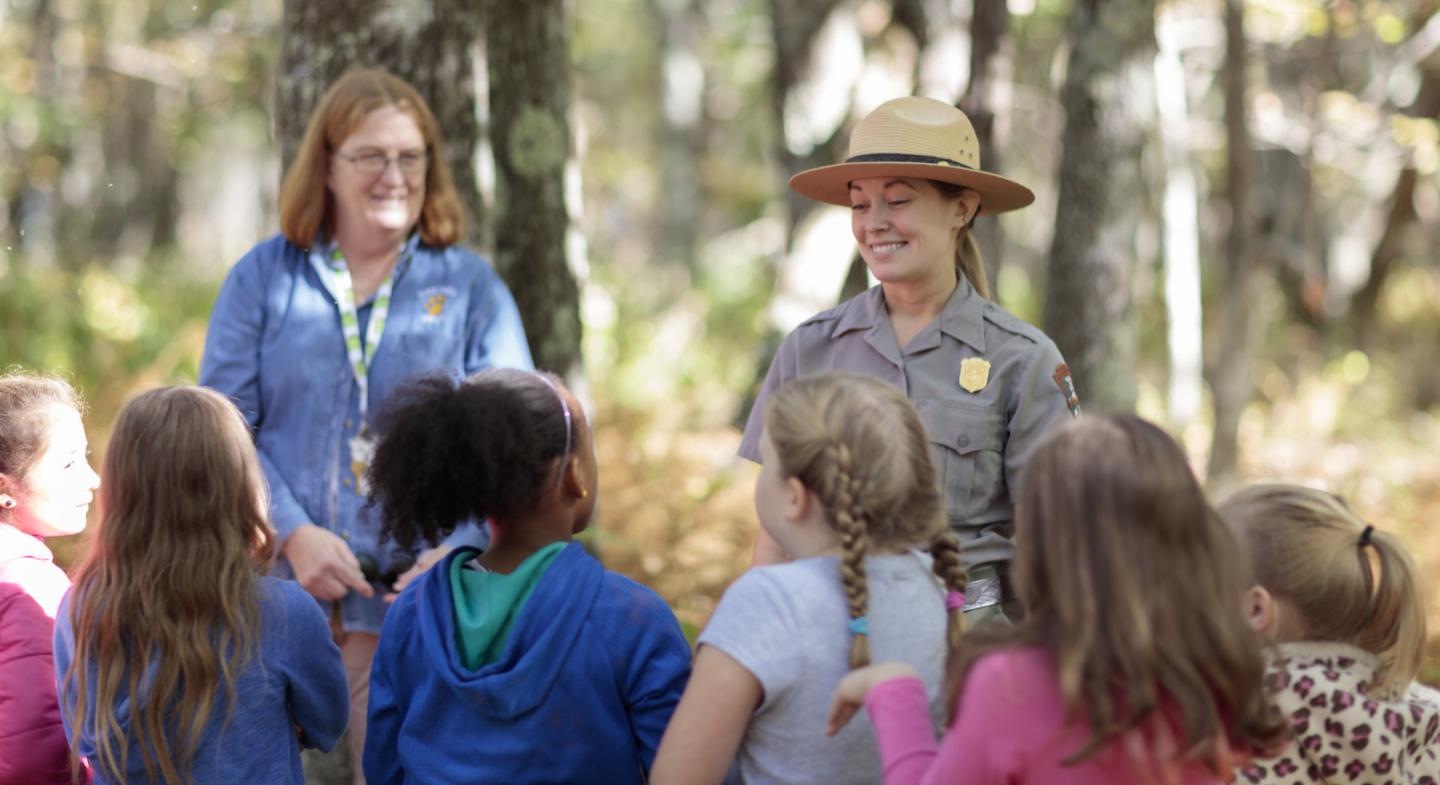 Park ranger and group of children in a forest setting.