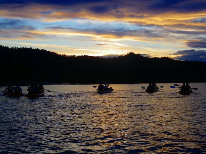 Kayakers on a lake at sunset, with dark silhouettes and vibrant sky.