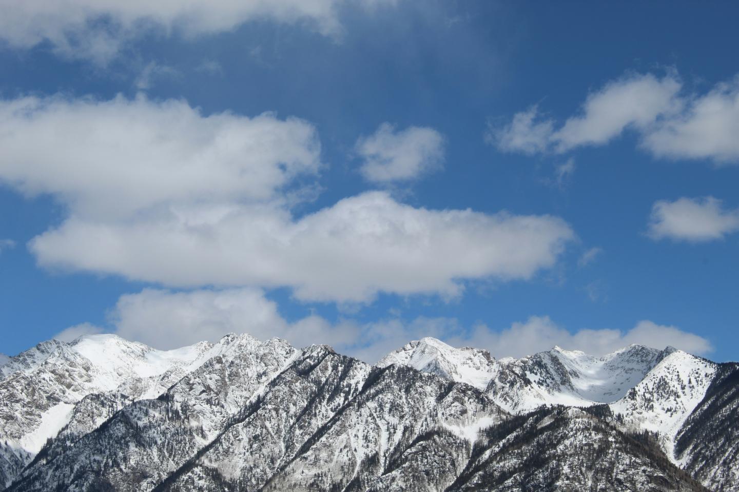 Snow-covered mountains under a blue sky with scattered clouds.