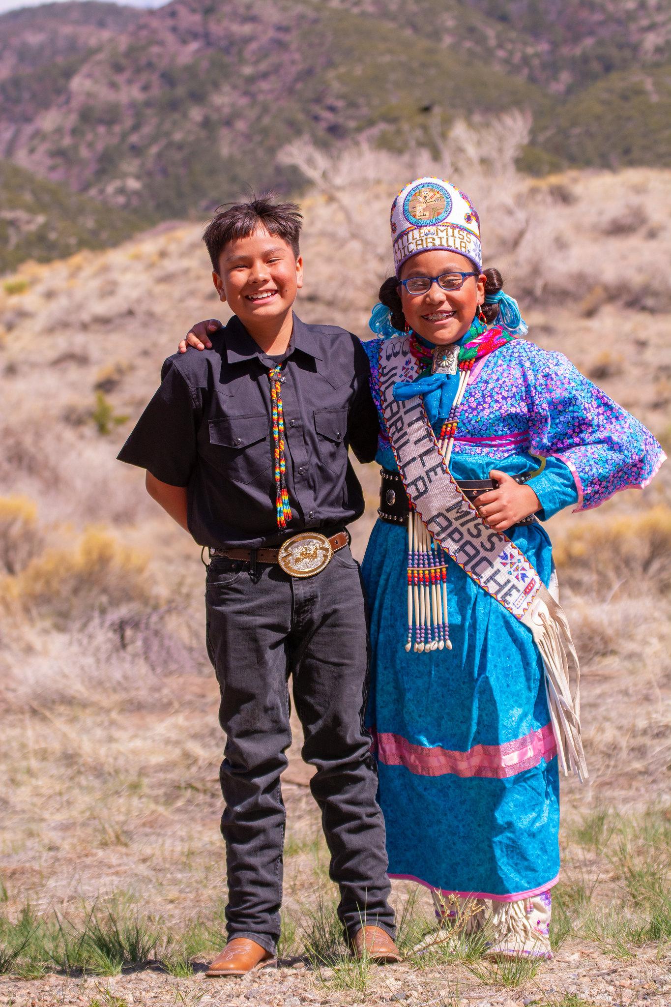Boy in black and girl in blue traditional attire smiling, standing in a field.