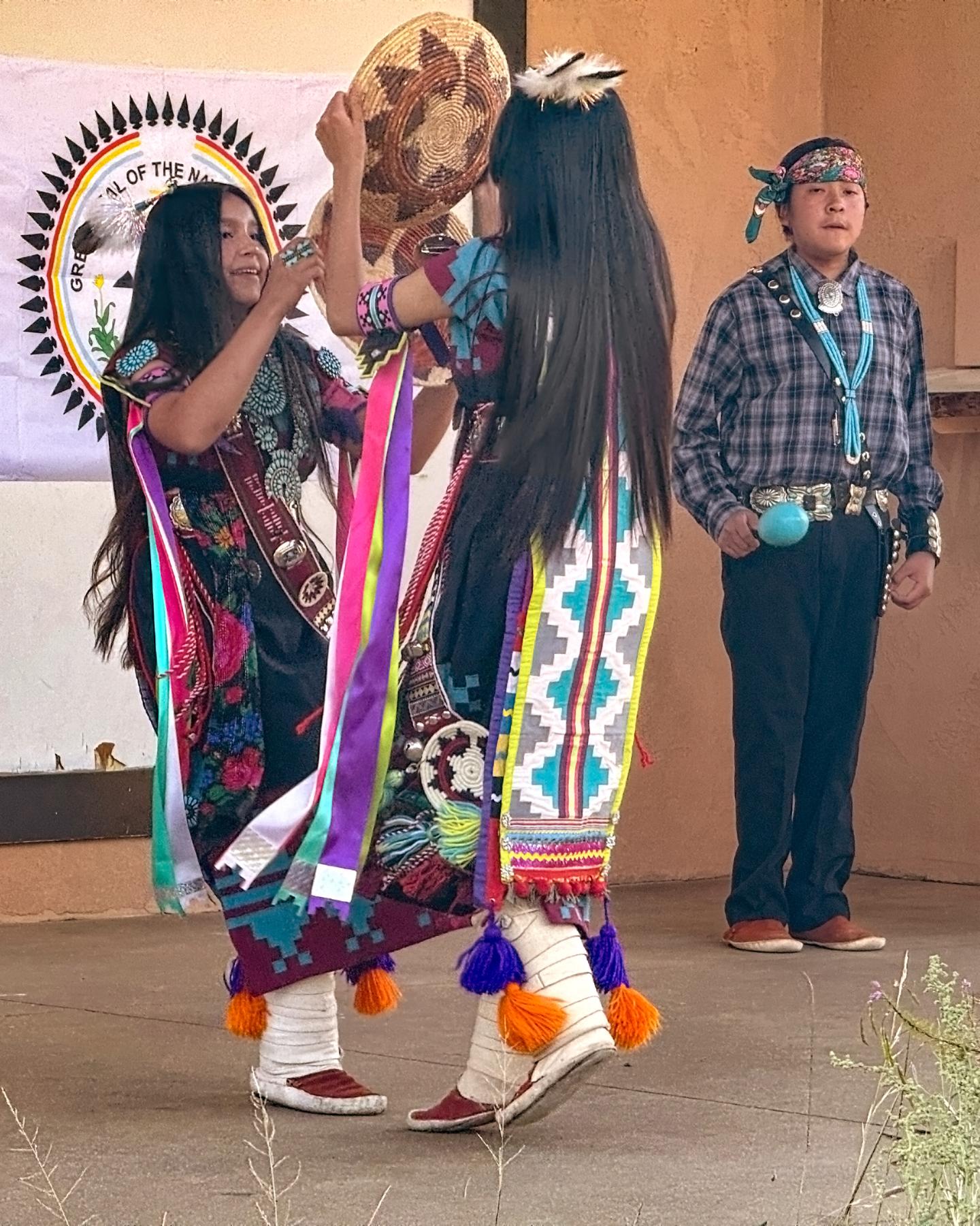 Dineh Tah dancers in traditional attire dancing, with one person holding a drum.