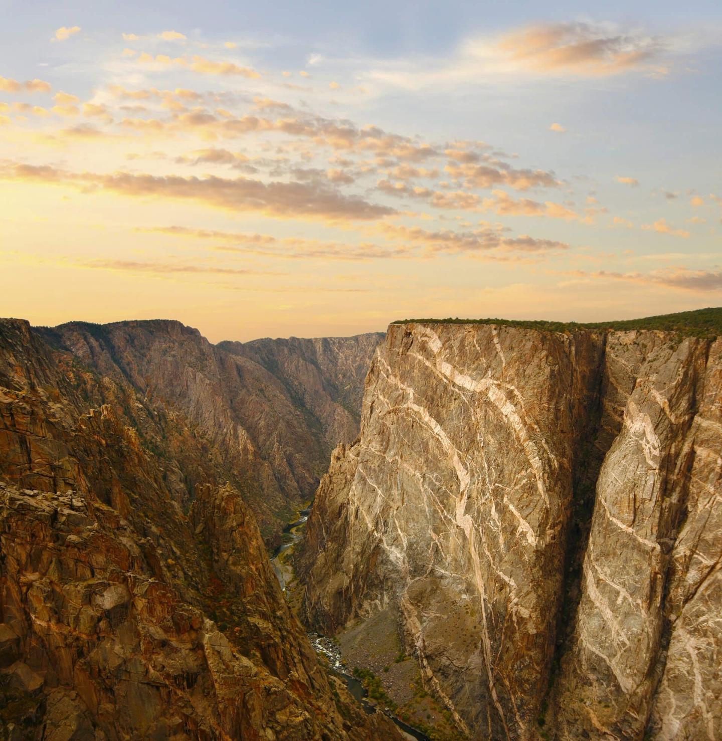 Canyon at sunset with steep cliffs and scattered clouds.