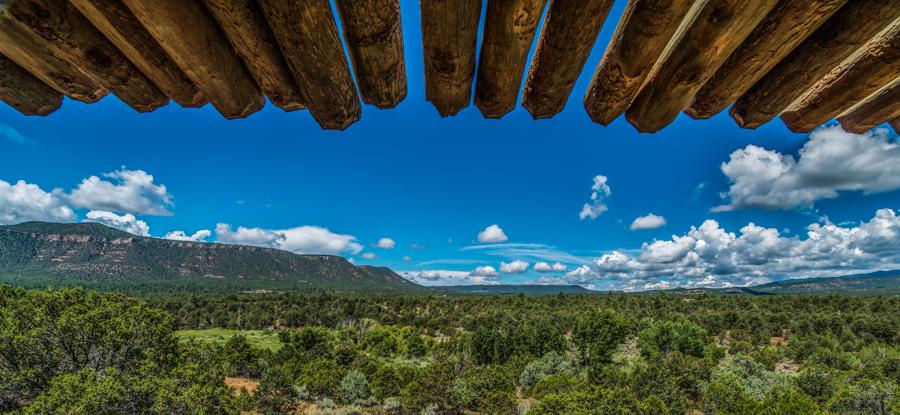 Wooden pergola over a vast green landscape and distant mountains under a blue sky.