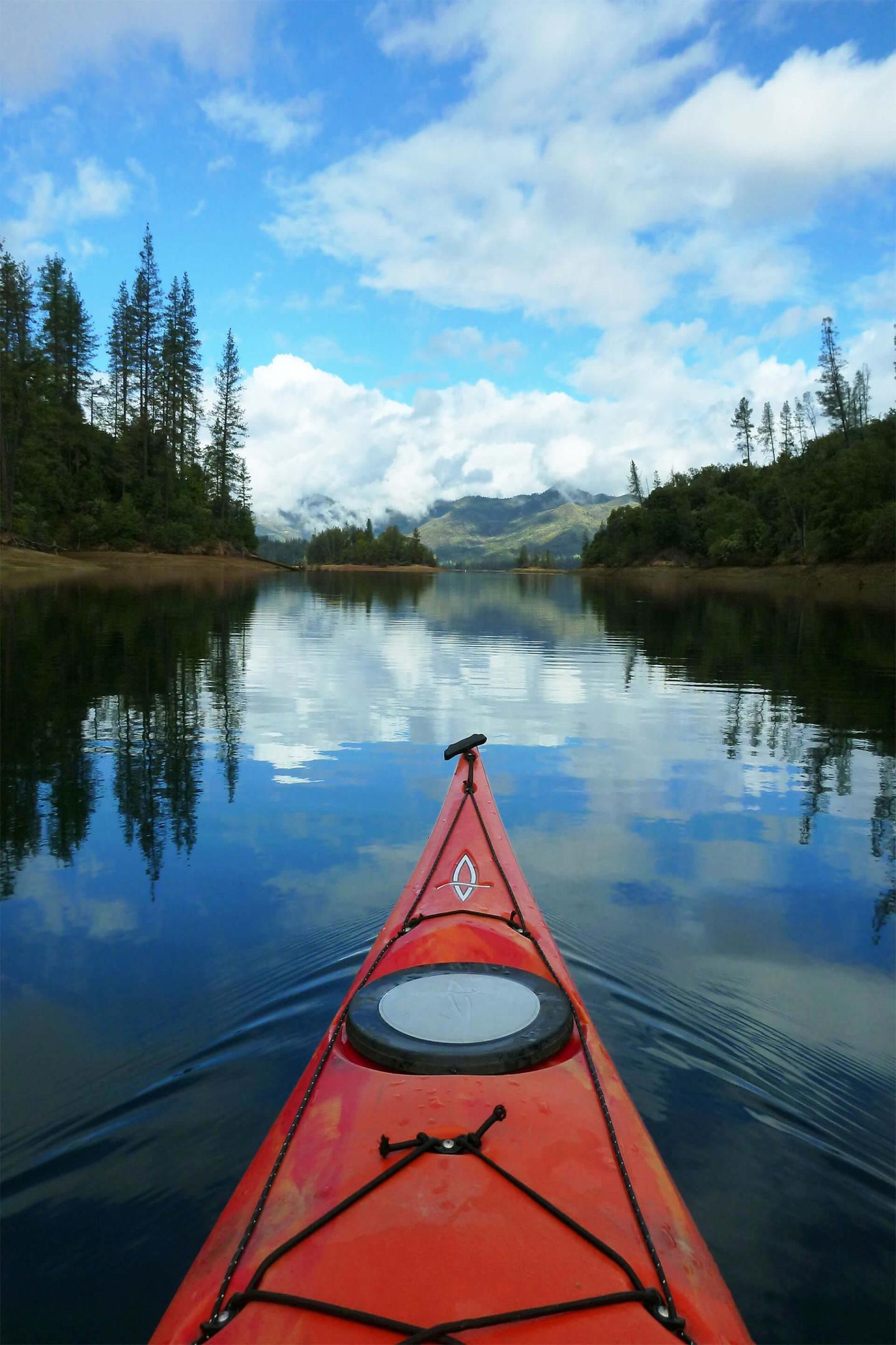 Red kayak on a calm lake with trees and mountains in the background.