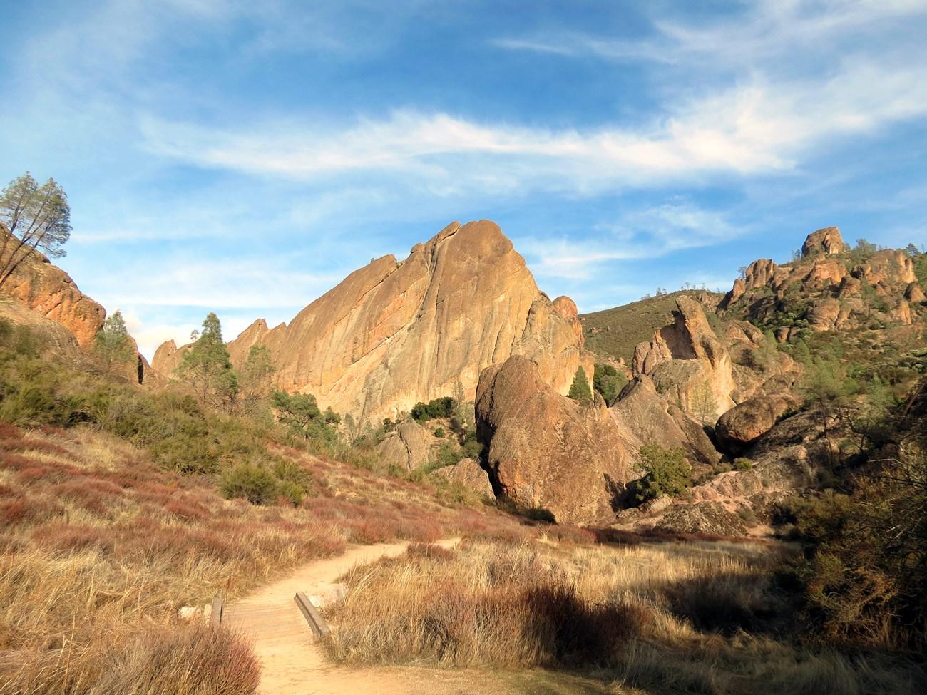 Pathway through rocky hills under a blue sky with scattered clouds.