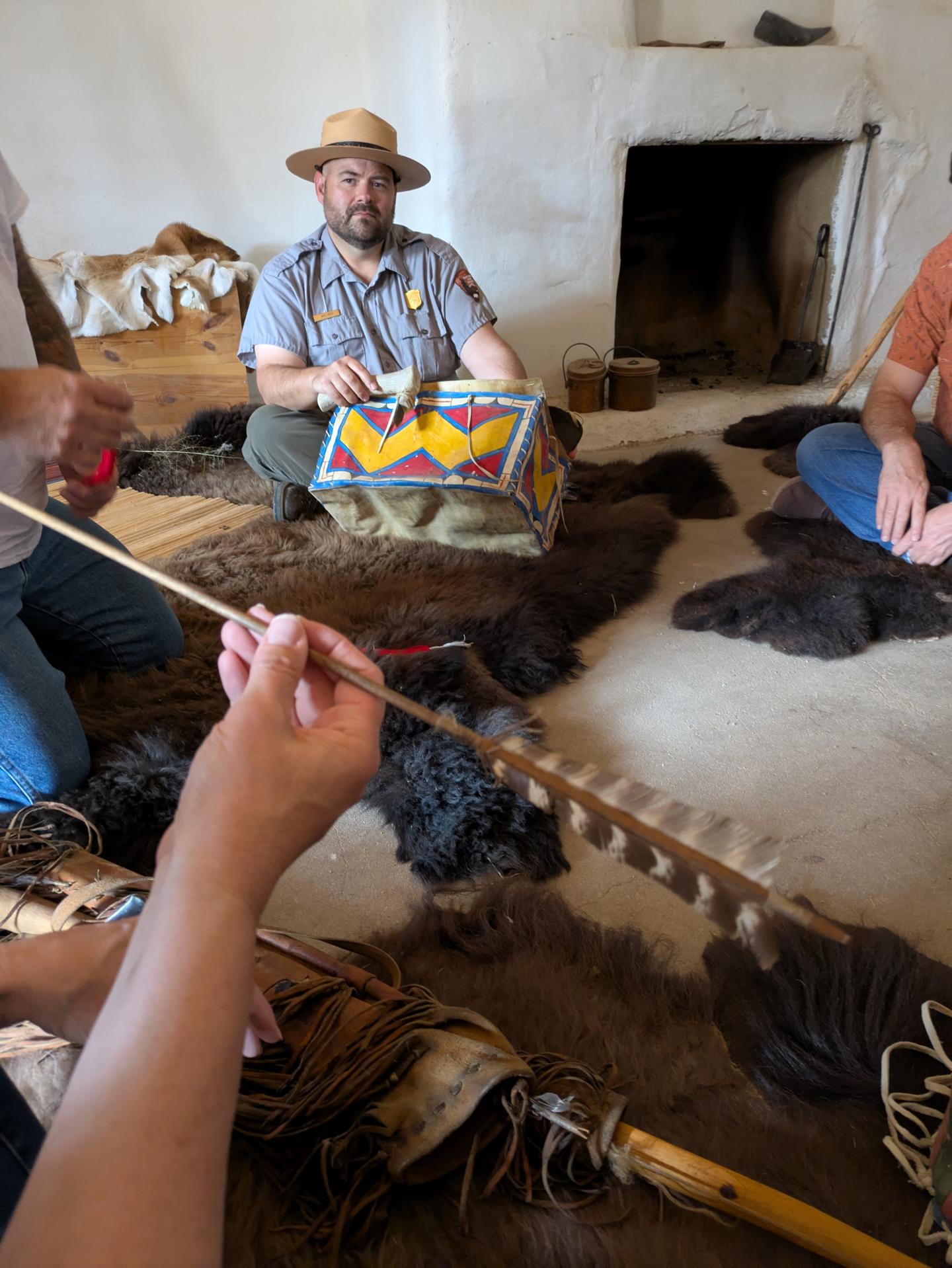 Historic reenactment with people crafting on a fur rug, one person holding a patterned drum.