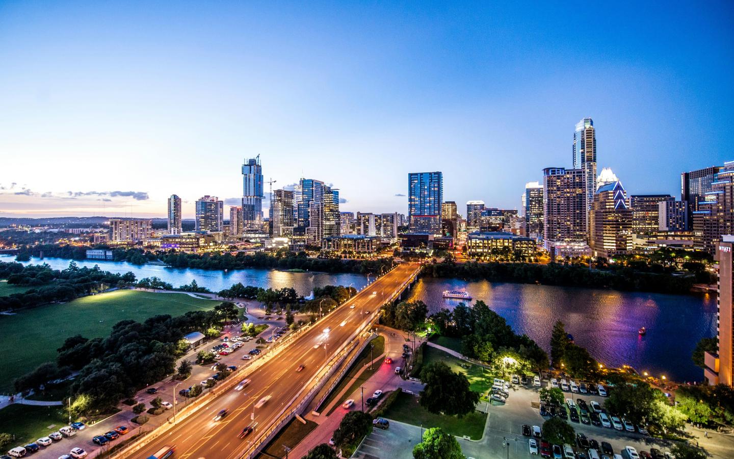 City skyline at dusk with a river and lit-up buildings.