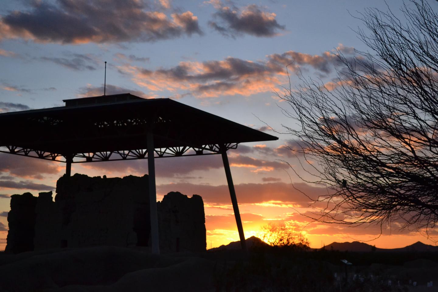 Sunset silhouette of ancient ruins and tree branches against an orange sky.