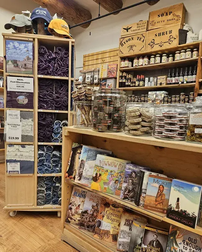 Store interior at Bent's Old Fort with shelves of books, hats, and various small packaged goods.