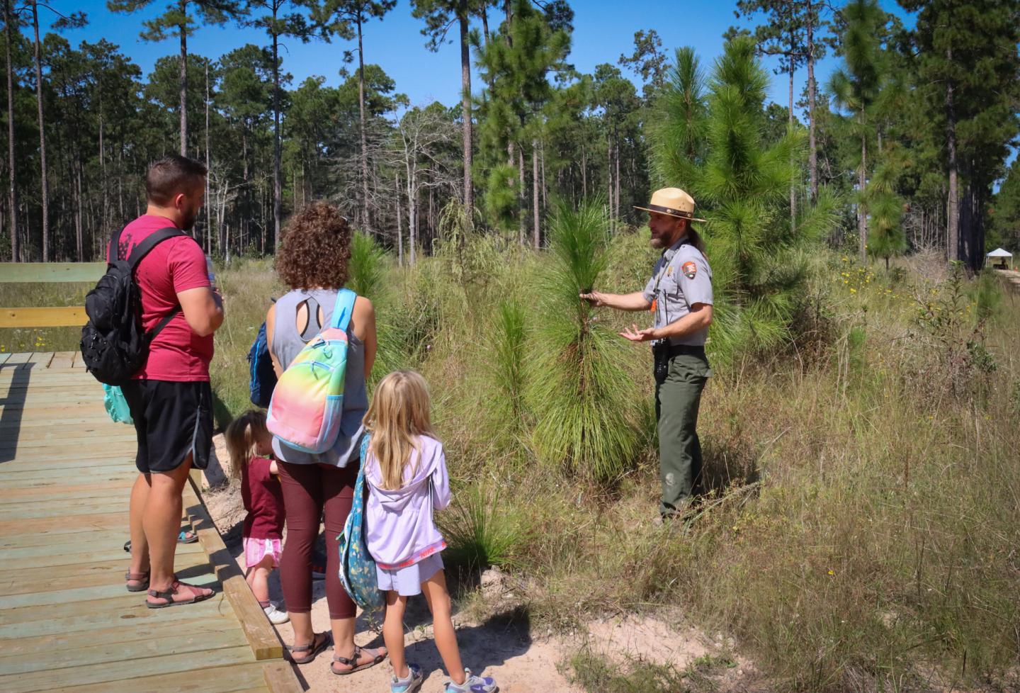 Park ranger explaining plants to a family in a wooded area.