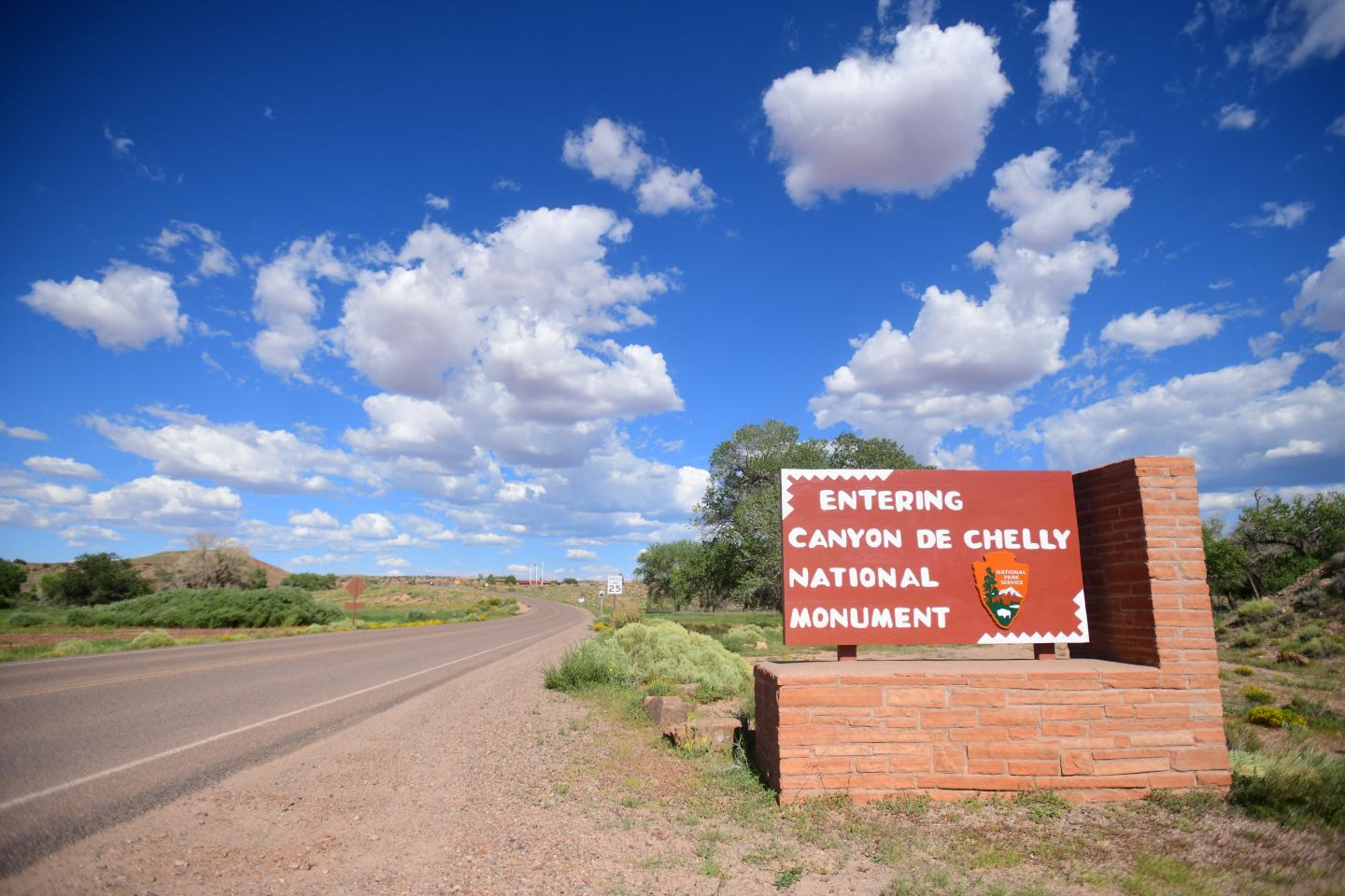 Entrance sign for Canyon de Chelly under a bright blue sky with clouds.