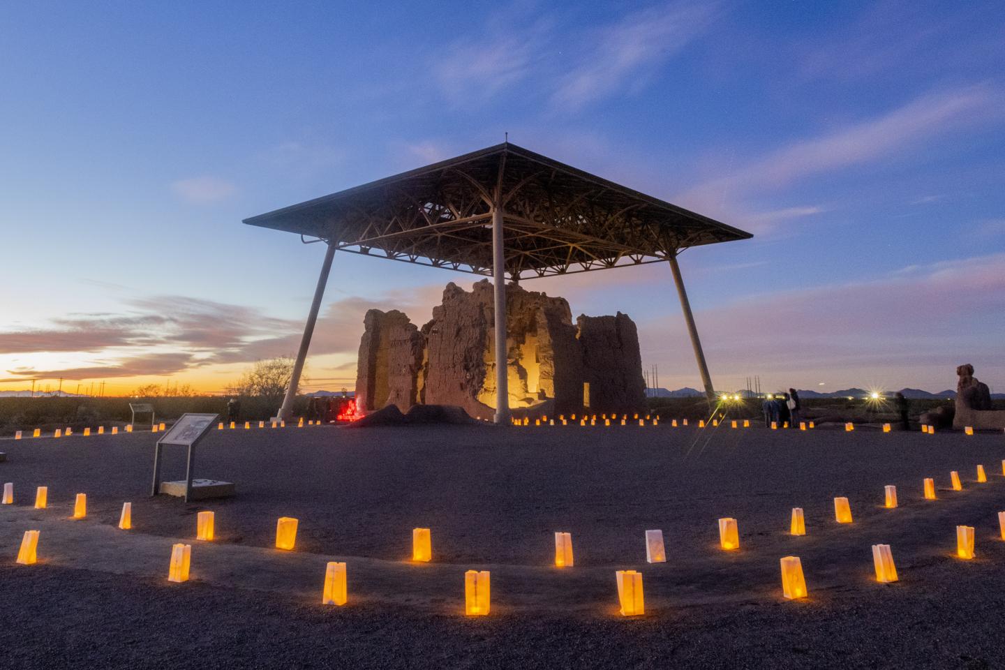 Casa Grande Ruins at sunset, surrounded by glowing luminaries.