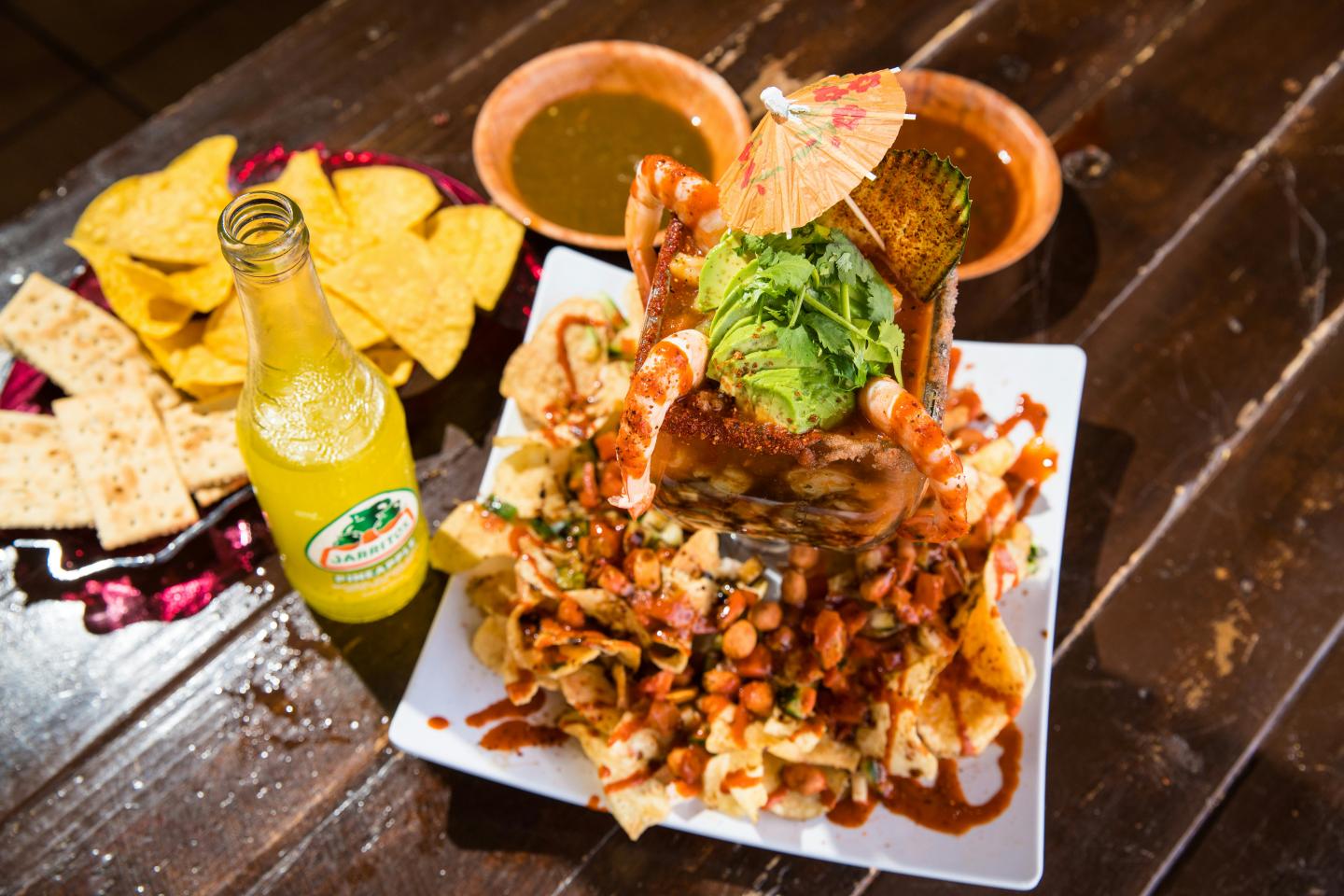Nachos with shrimp, avocado, and sauce, served with chips and a bottle of soda.