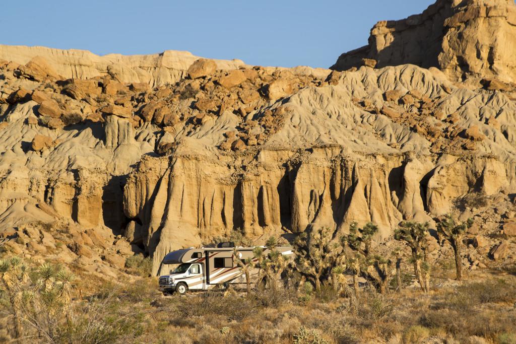 RV parked in a desert landscape with rocky cliffs and cacti.
