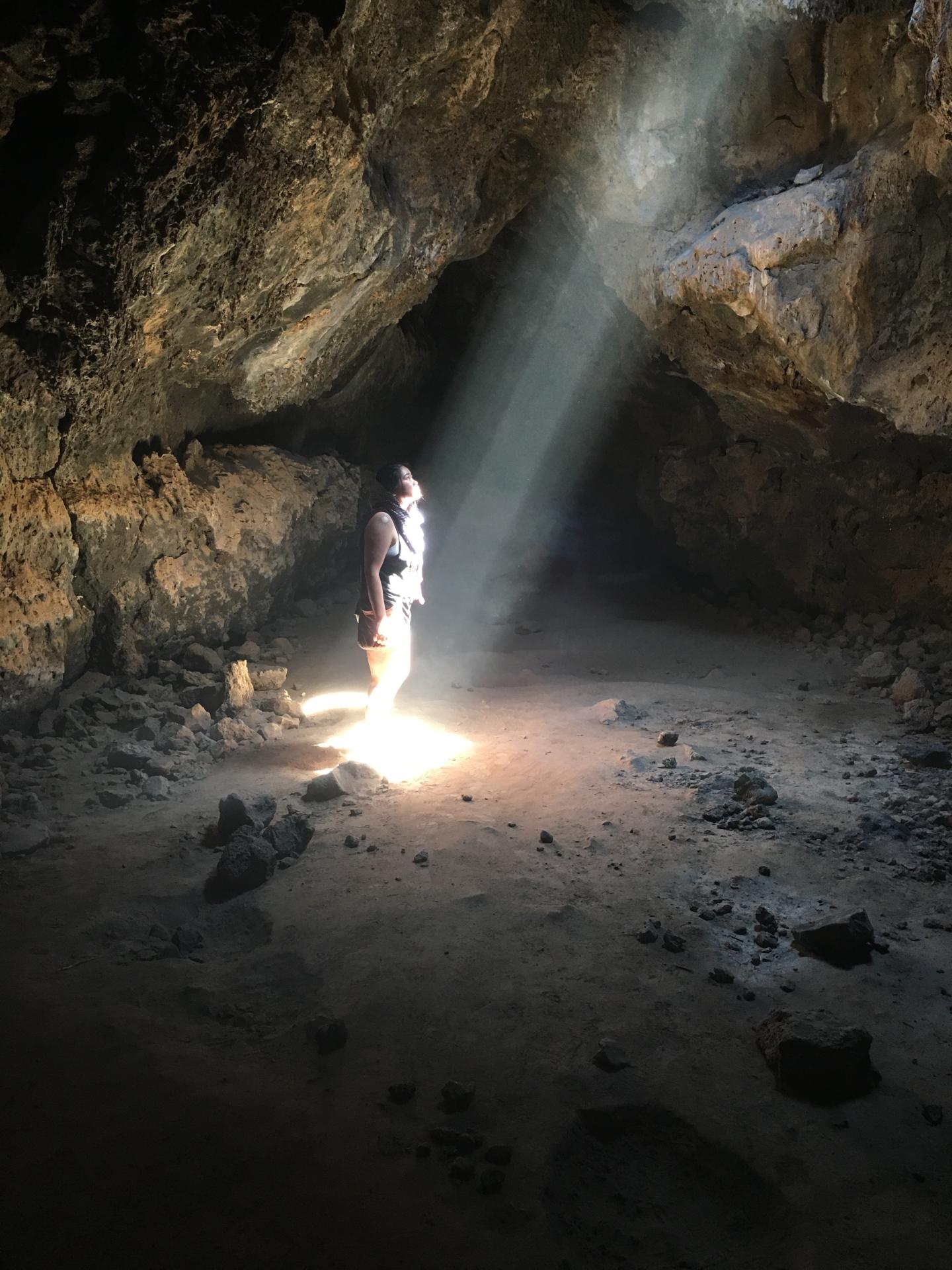 Person standing in a cave, illuminated by a beam of sunlight.
