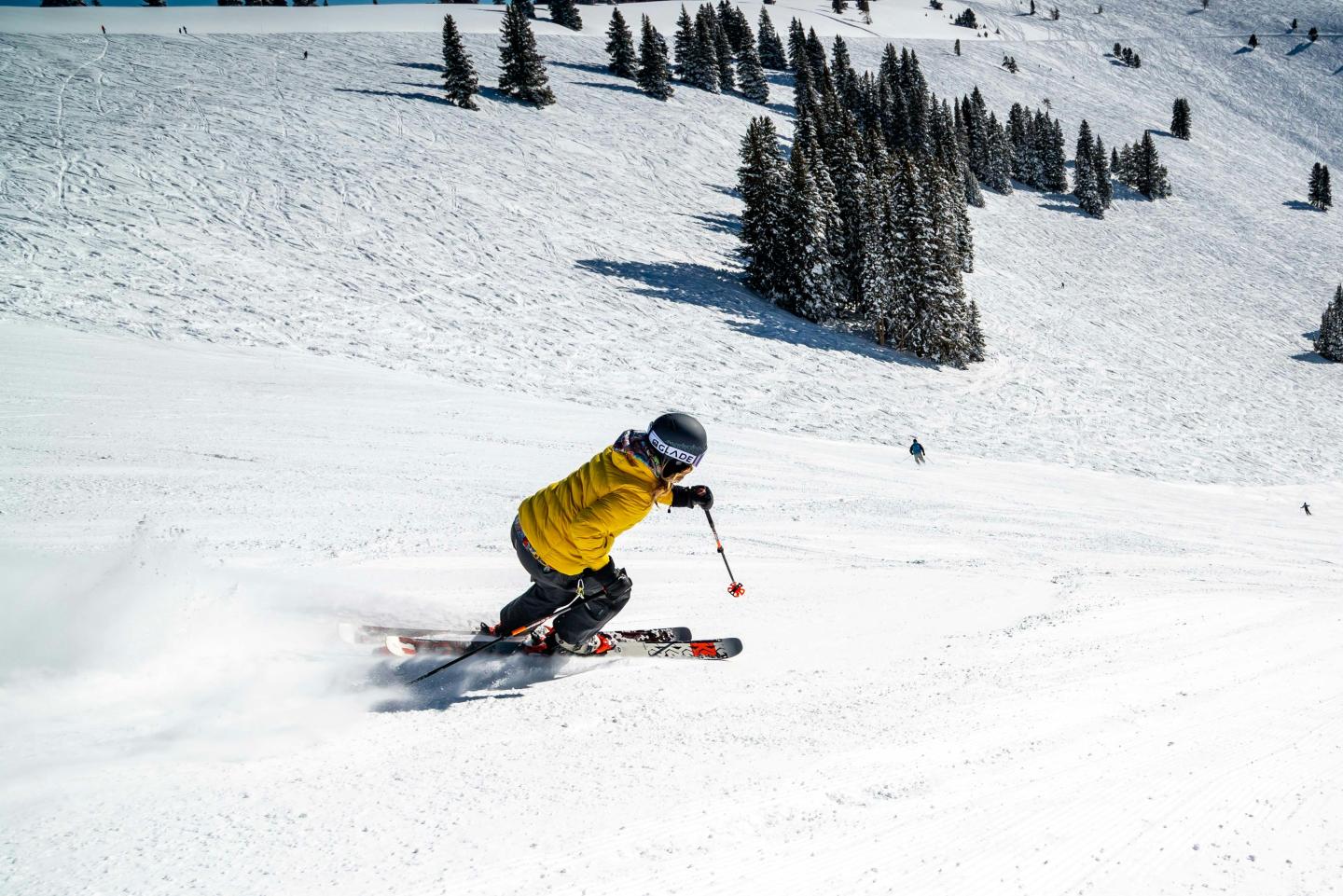 Skier in yellow descends snowy slope with trees in the background.
