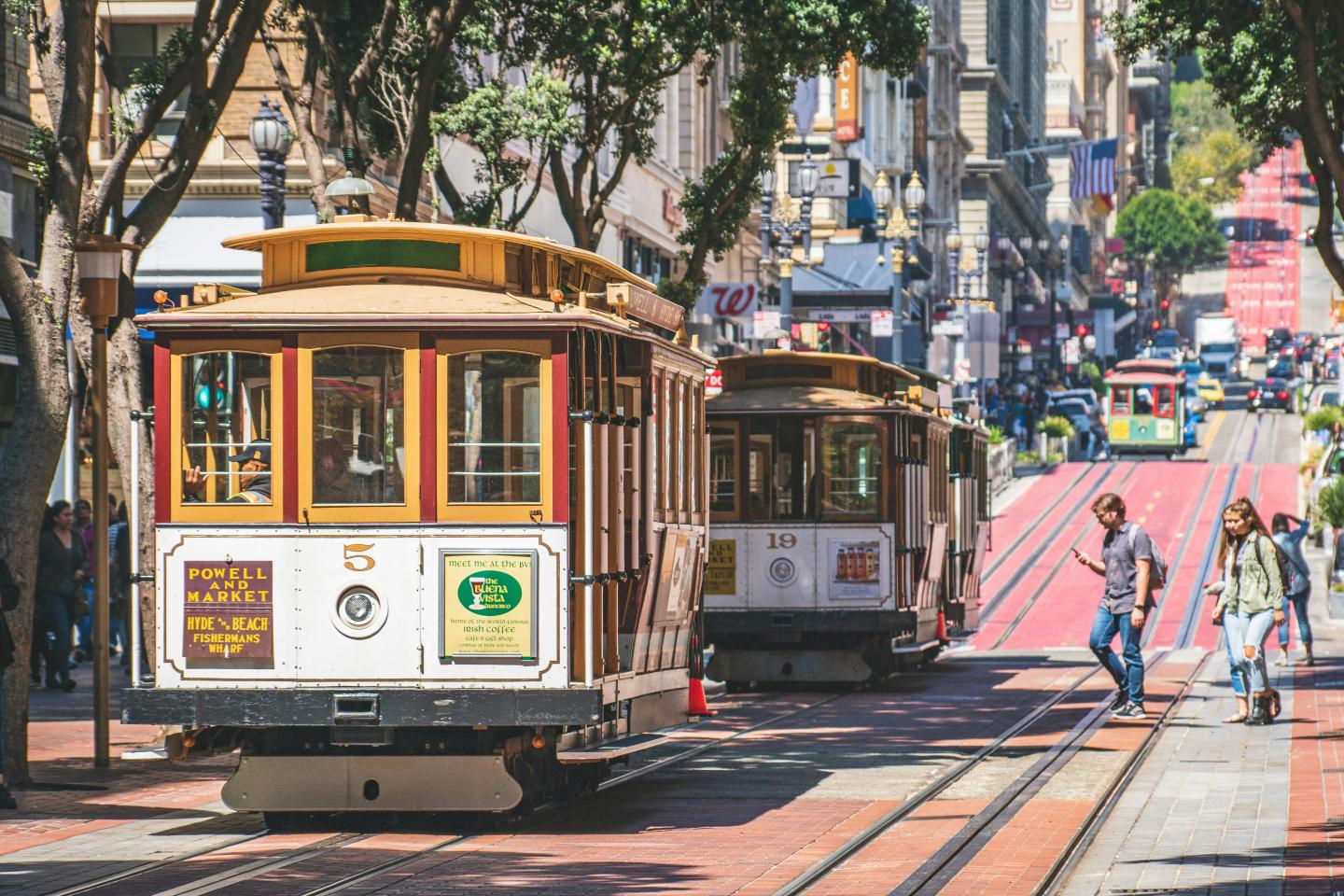 Cable cars on a bustling city street, people crossing the tracks.