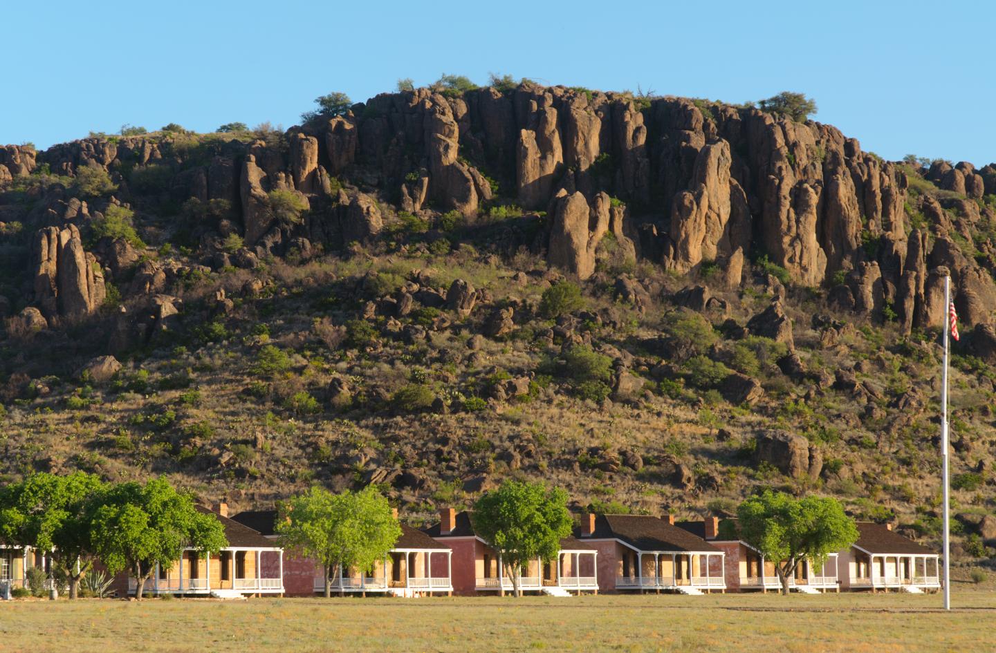 Row of houses under a rocky cliff with clear blue sky.