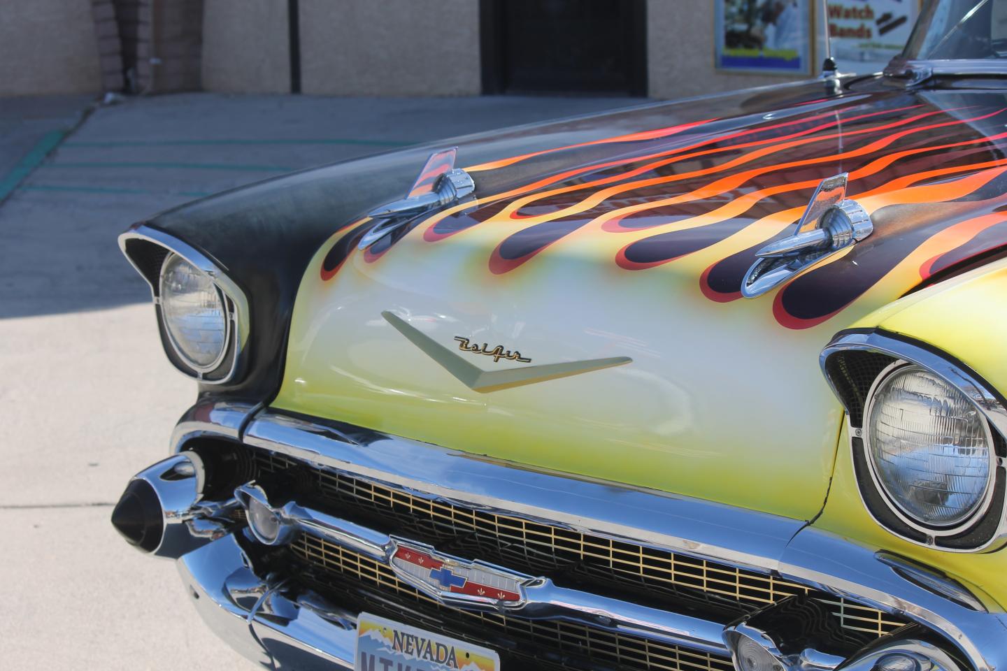 Vintage car with a flame-painted hood, shiny chrome bumper, and classic headlights.