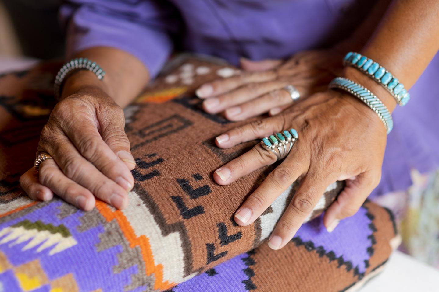 Hands wearing turquoise jewelry touch a patterned woven blanket.