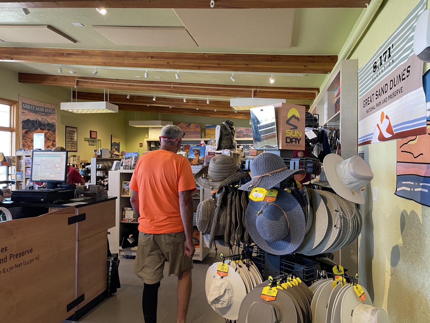 Man in orange shirt shopping for hats in the park store at Great Sand Dunes National Park.