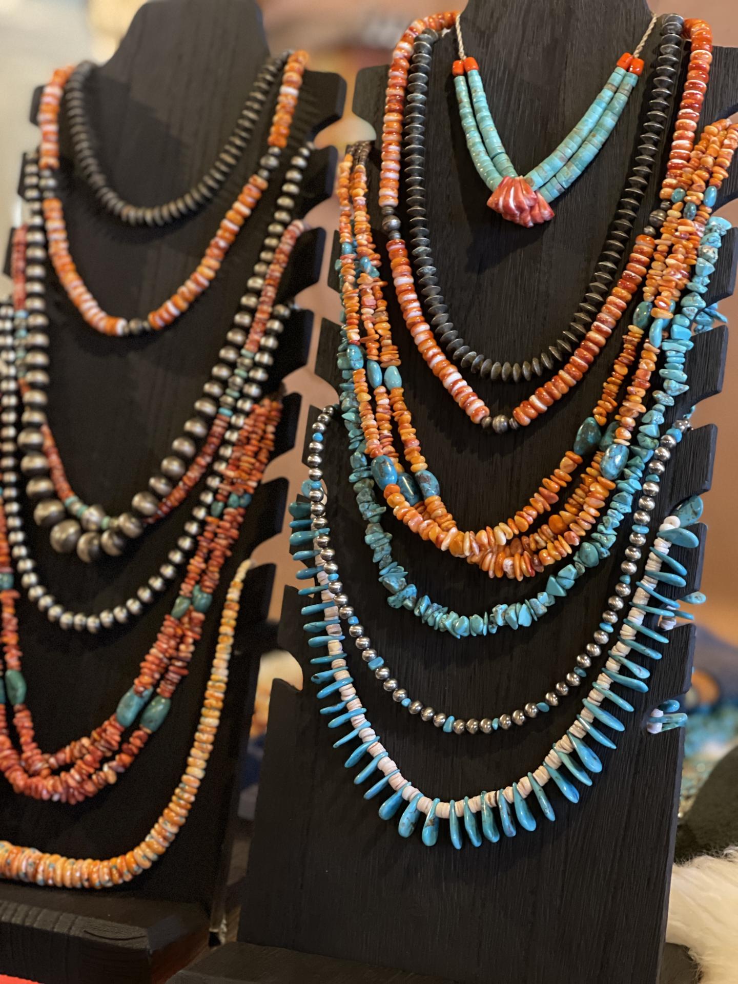 Colorful turquoise and coral necklaces displayed on black stands.