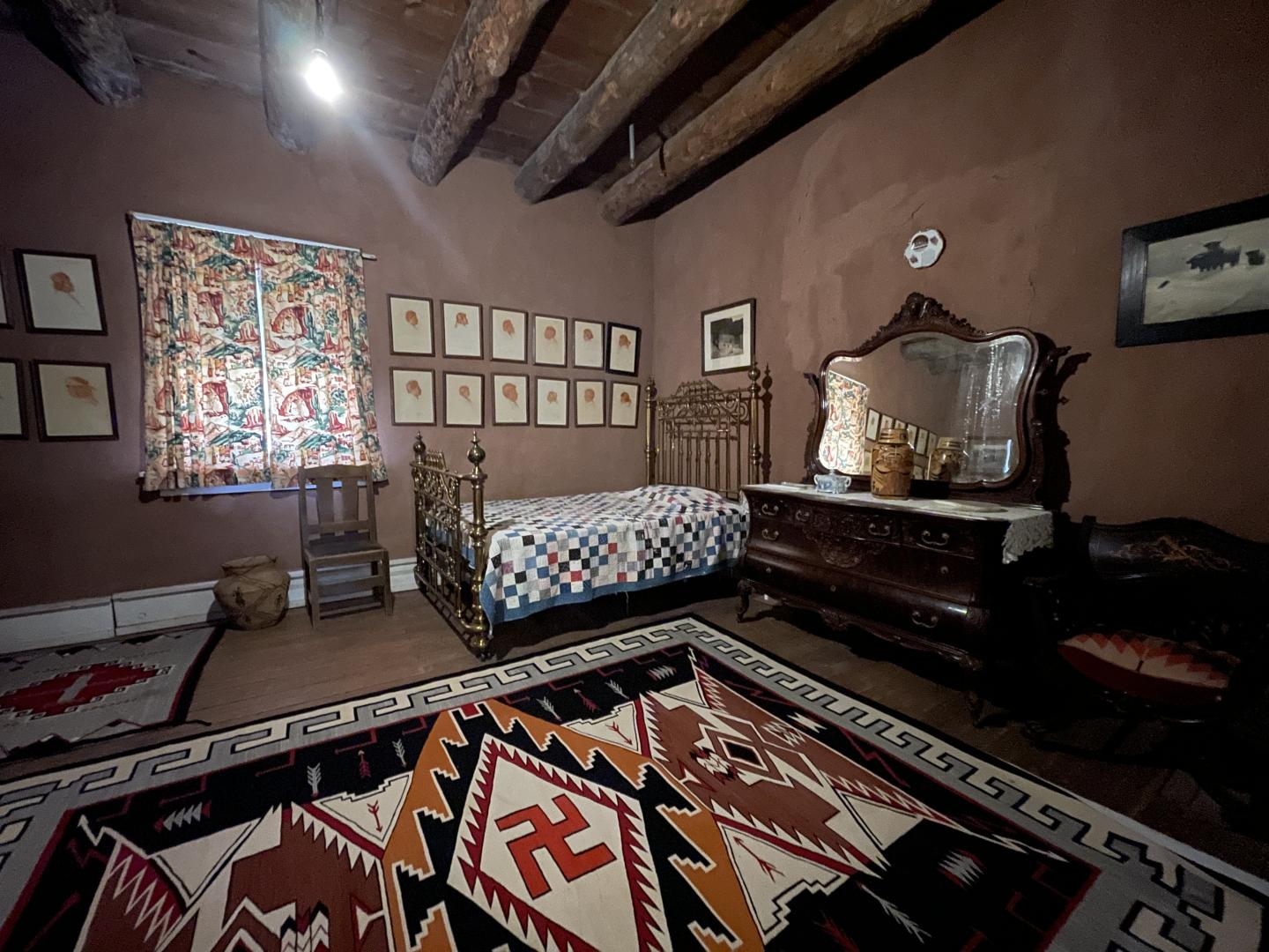 Historic Hubbell bedroom with wooden beams, a single bed, vintage furniture, and patterned, woven, Navajo rug.