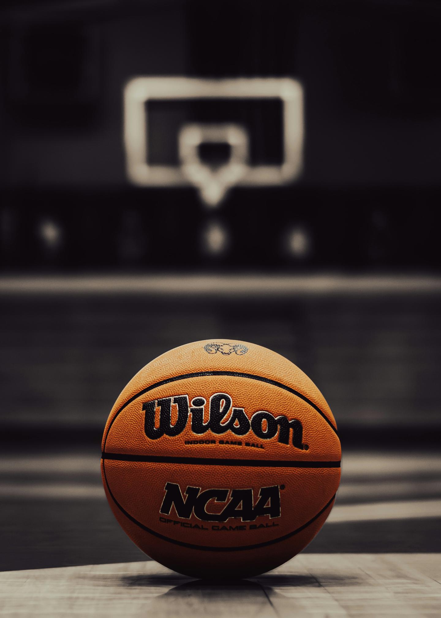 Basketball on court with hoop in background, dimly lit.