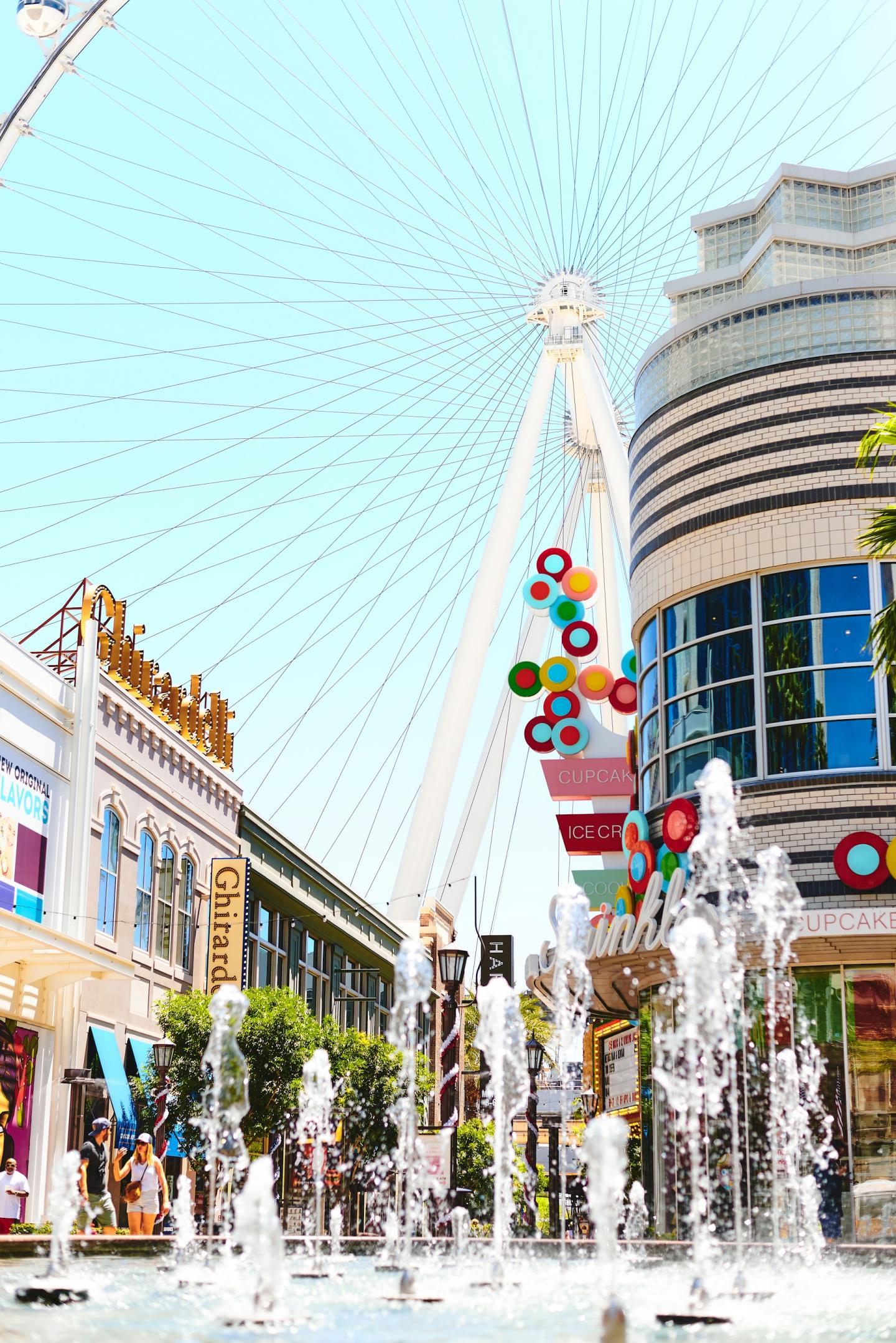 Fountain and Ferris wheel beneath a clear blue sky in a cityscape.