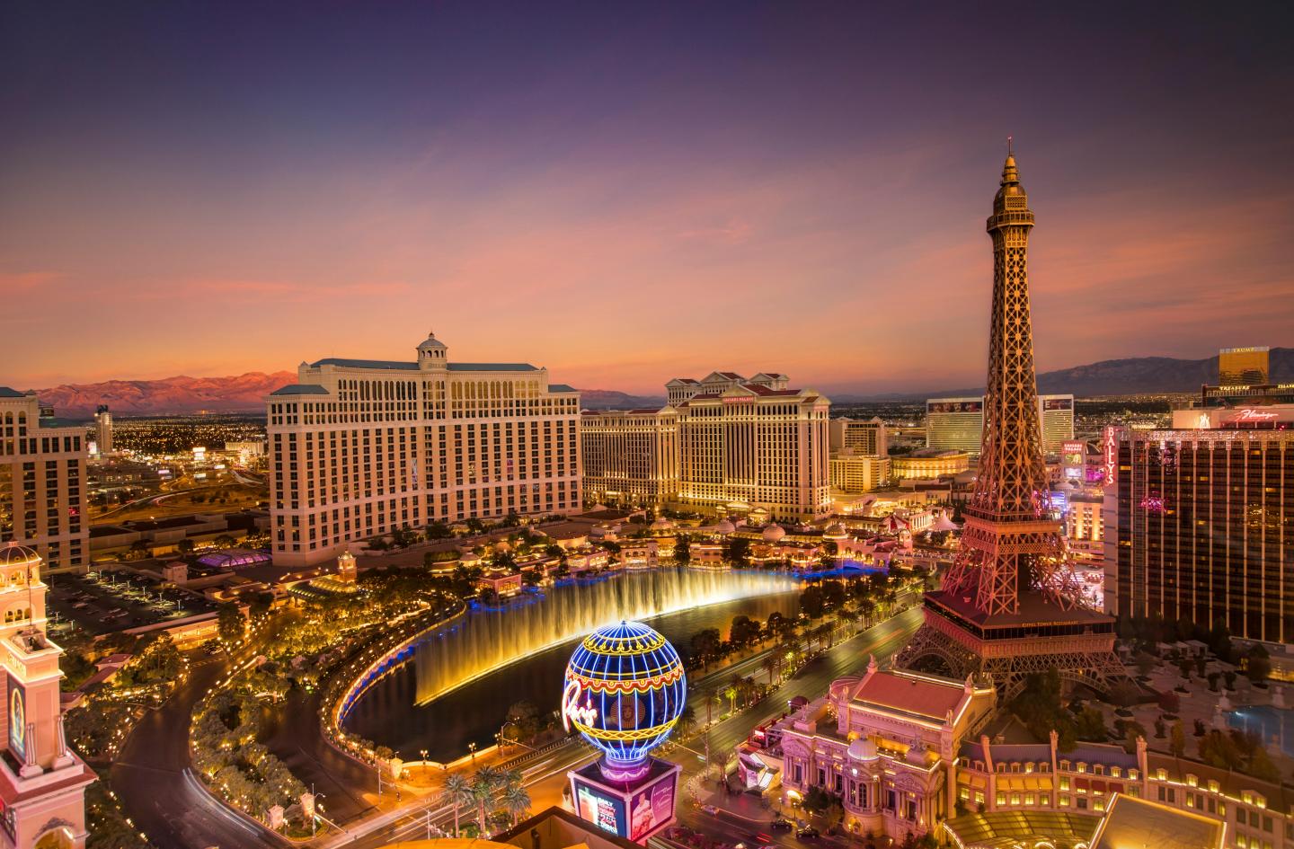 Las Vegas Strip at sunset with illuminated buildings and Eiffel Tower replica.